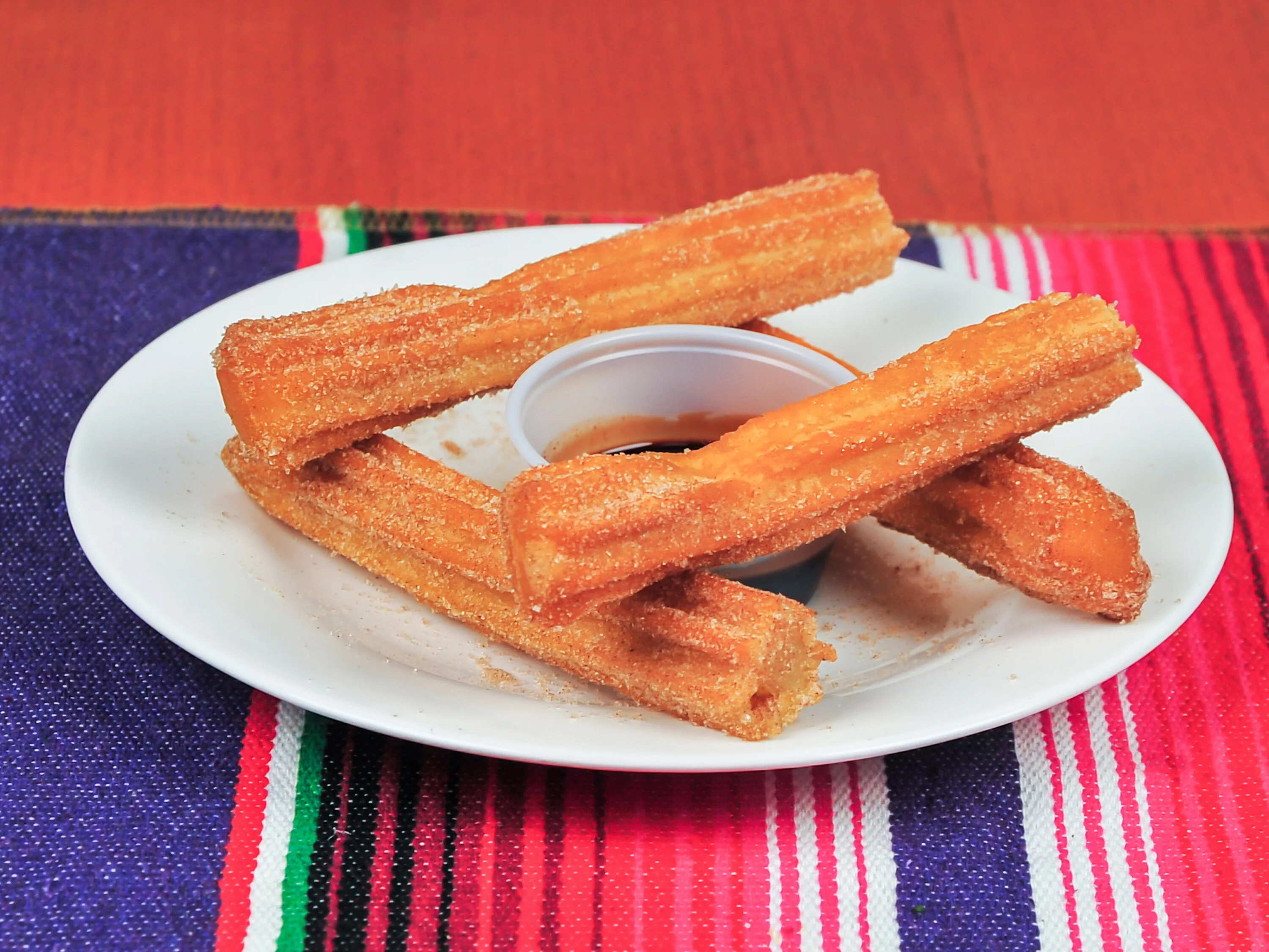 A plate of churros coated in sugar, served with a small container of chocolate sauce for dipping.