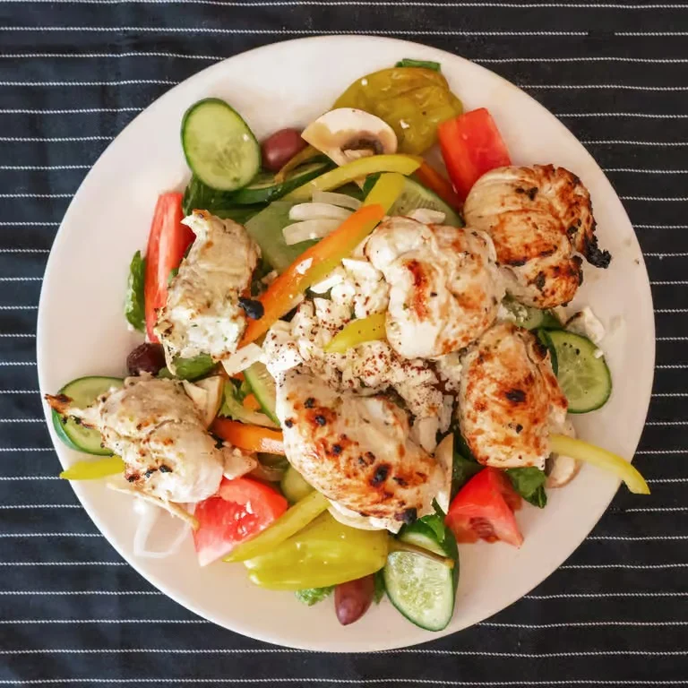 Grilled chicken salad with fresh vegetables on a white plate.