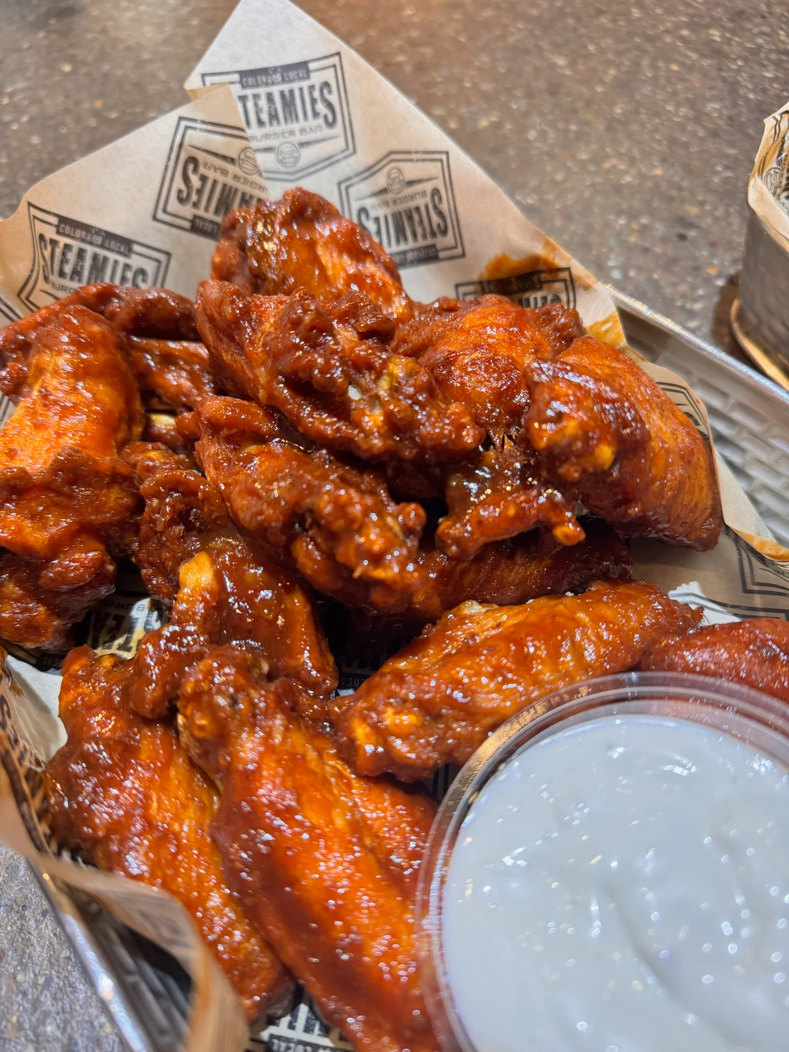 A plate of spicy chicken wings glistening in a rich sauce, accompanied by a small cup of dipping sauce.