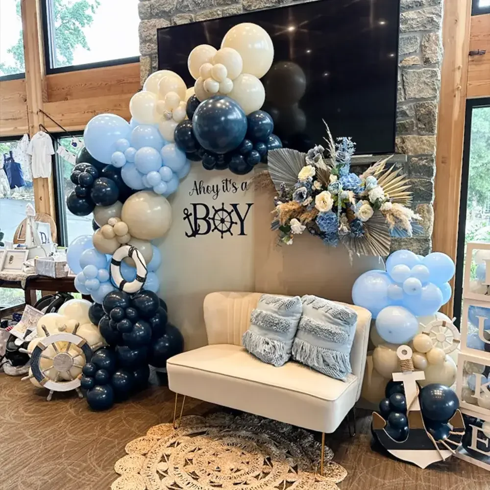 A vibrant decoration setup for a baby boy celebration, featuring an array of blue and neutral colored balloons, along with floral accents and a welcoming sign.