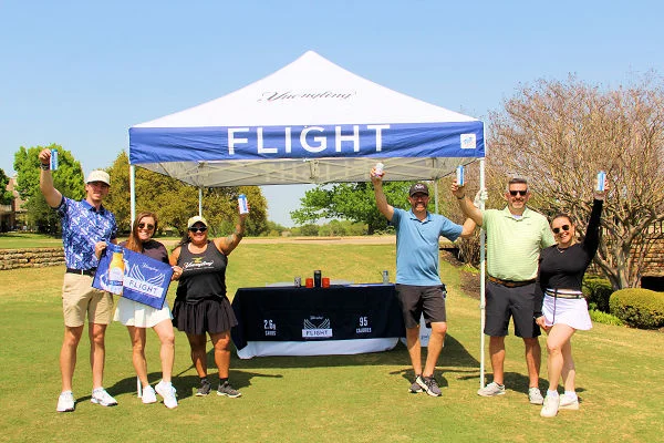 Group celebrating at a branded outdoor event tent on a sunny golf course
