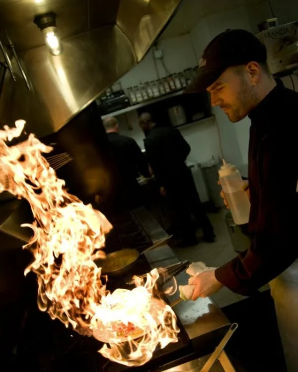 Chef flambéing a dish in a busy restaurant kitchen.