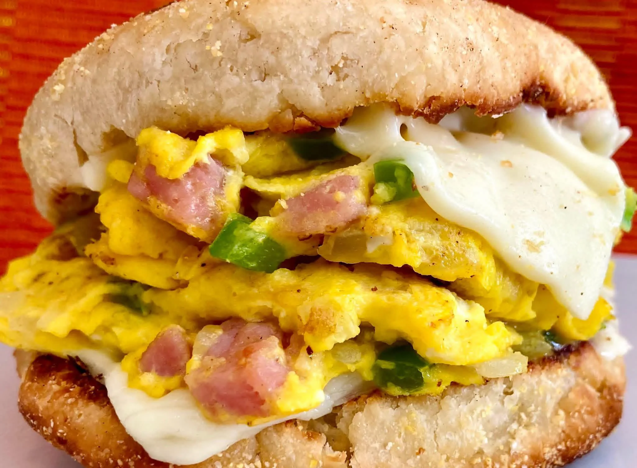 A sandwich filled with scrambled eggs, ham, and cheese, served on a toasted bun.