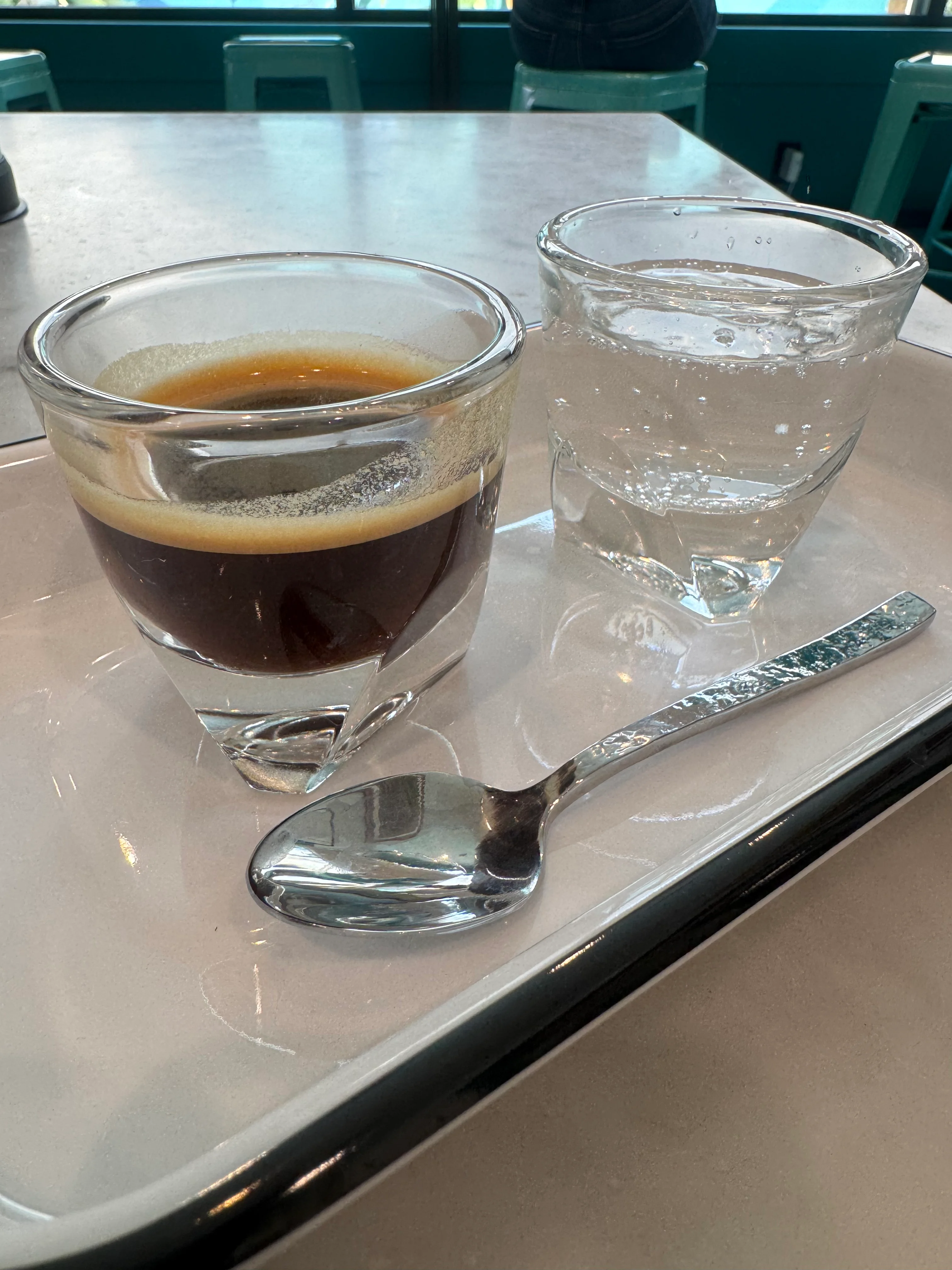 A close-up view of a coffee shot served with a glass of water on a tray, showcasing the rich color and texture of the espresso.