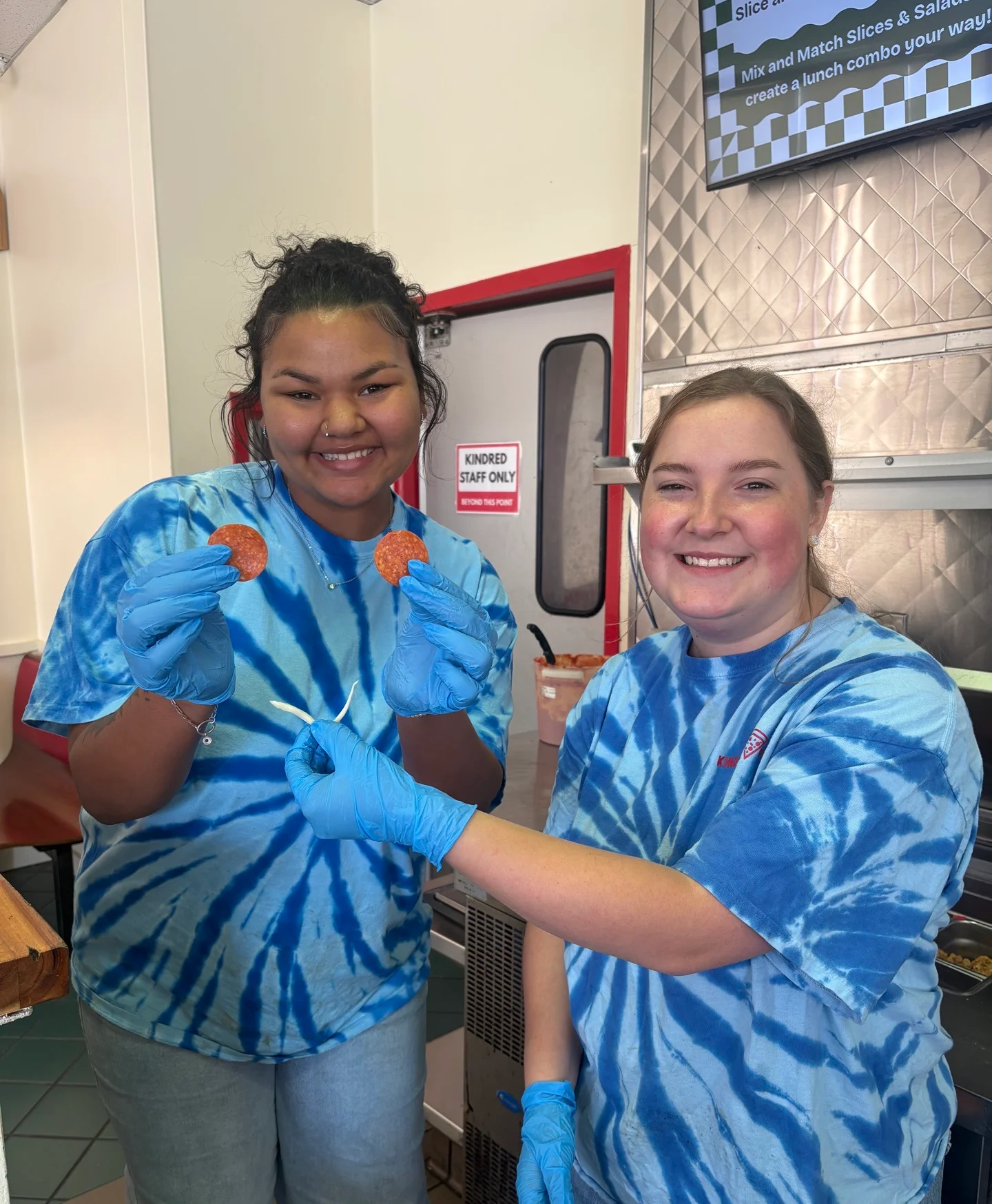 Two staff members showcasing pepperoni slices in a vibrant restaurant setting
