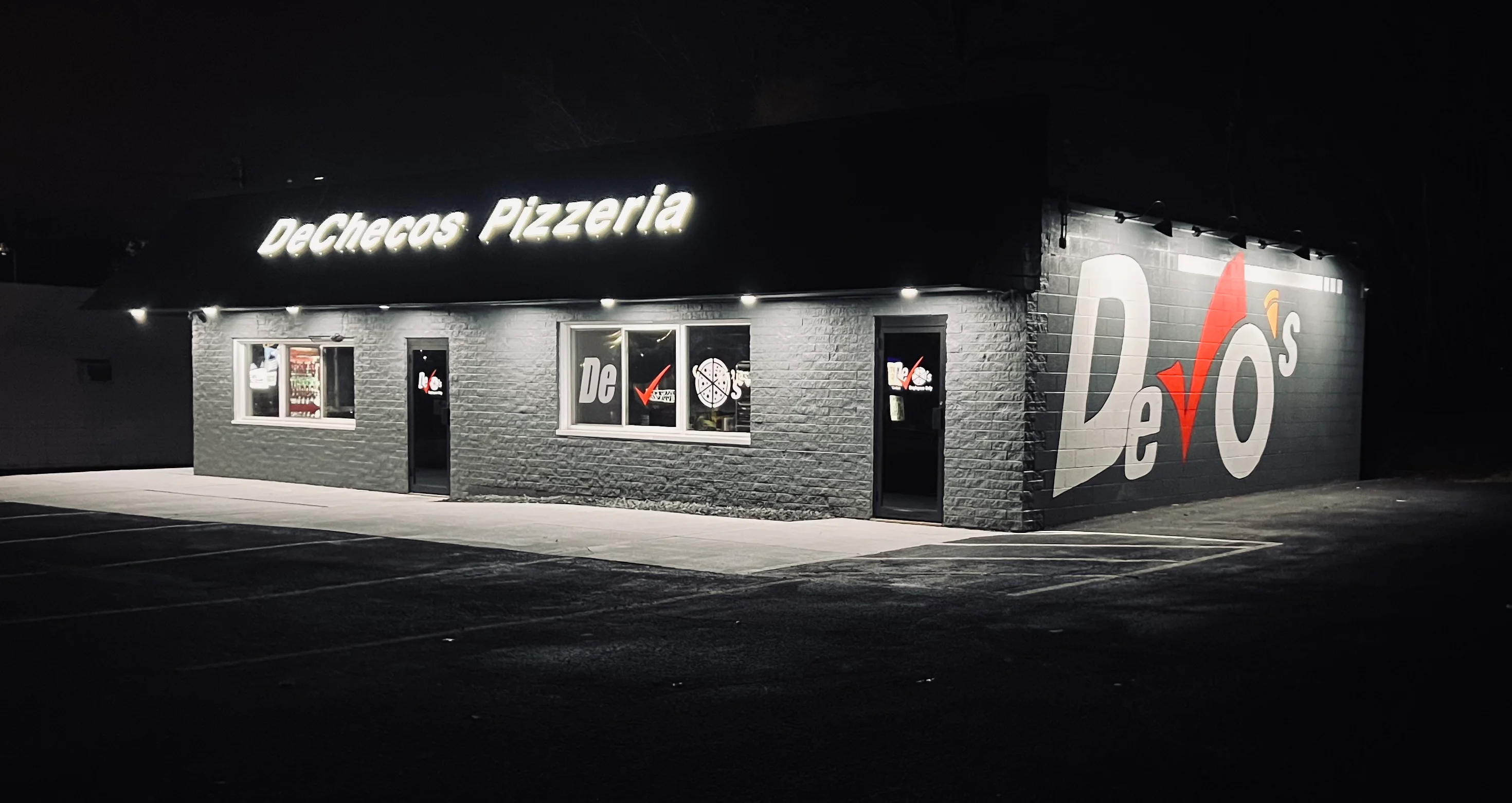 Exterior view of DeChecos Pizzeria at night with illuminated signage