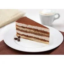 A slice of layered cake with creamy fillings, resting on a white plate next to a cup of coffee.