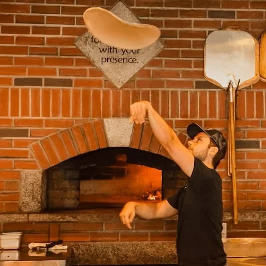 Pizza chef tossing dough in a brick oven restaurant.