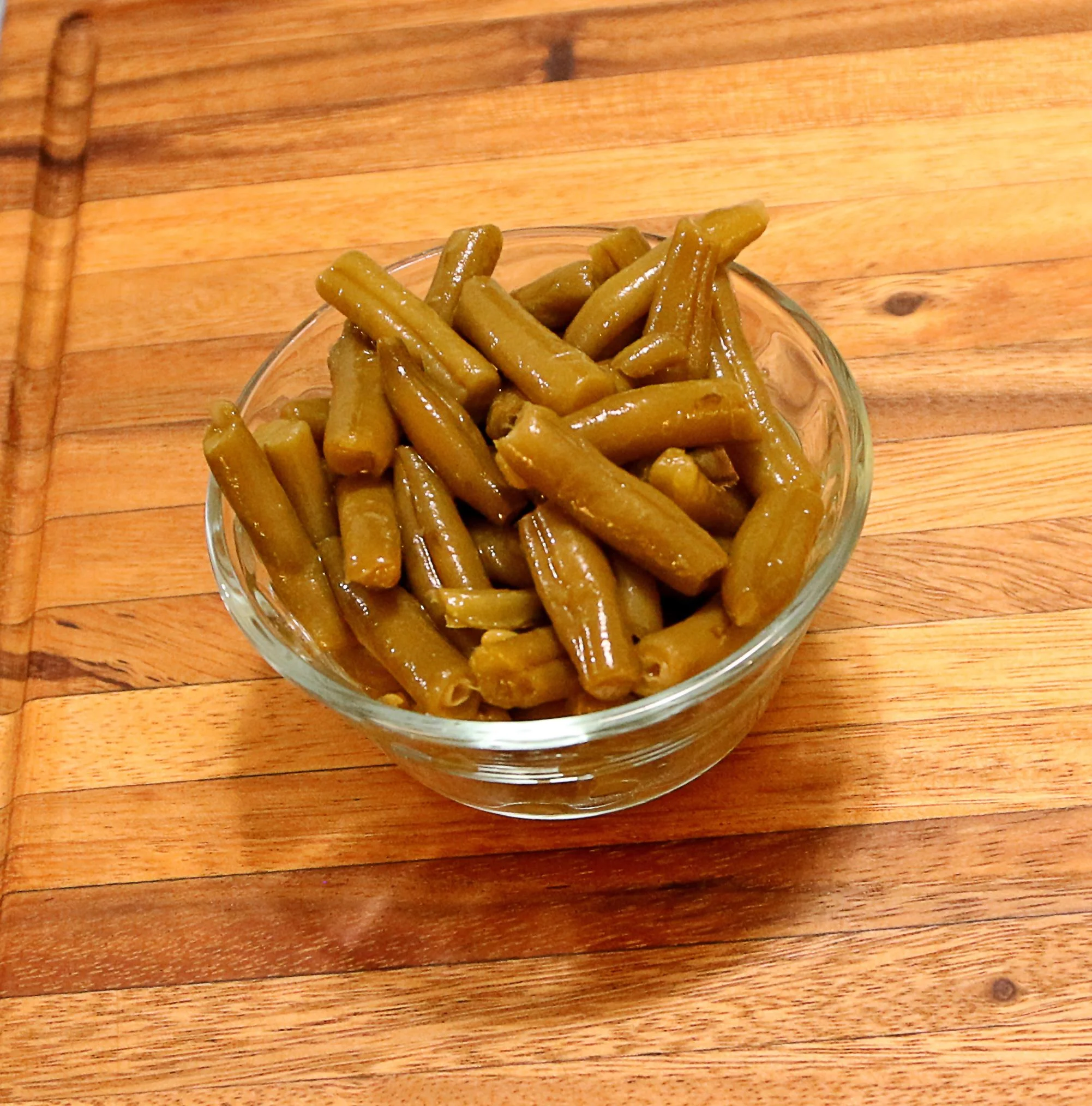 A glass bowl filled with cooked green beans, neatly arranged.