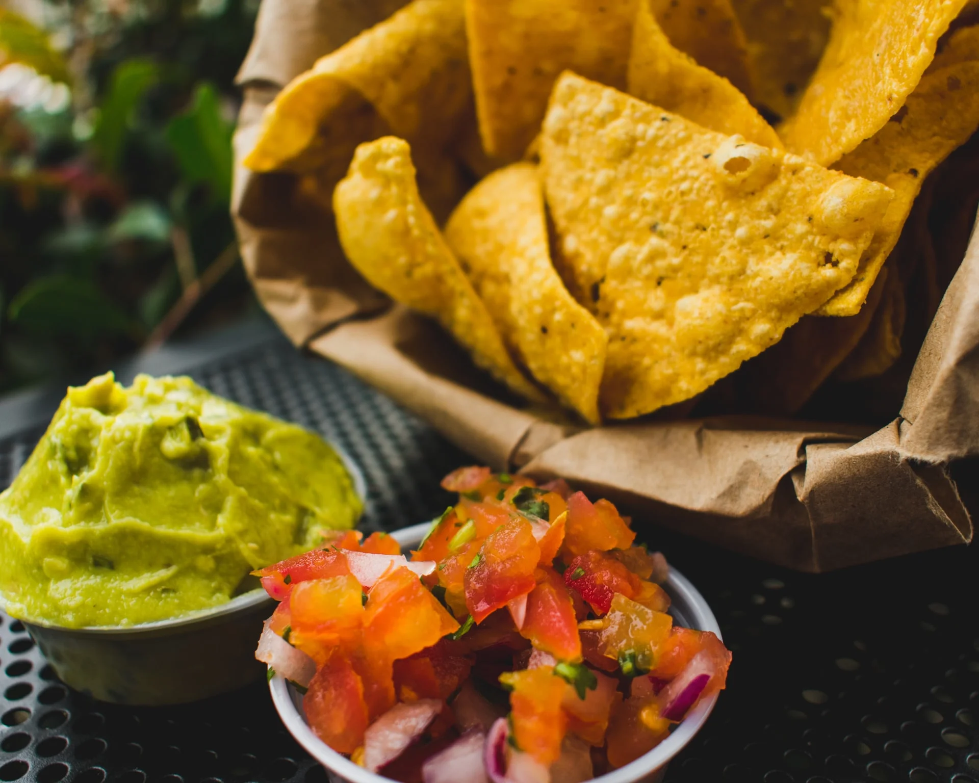 A serving of tortilla chips accompanied by guacamole and fresh salsa. The chips are arranged in a paper-lined basket.