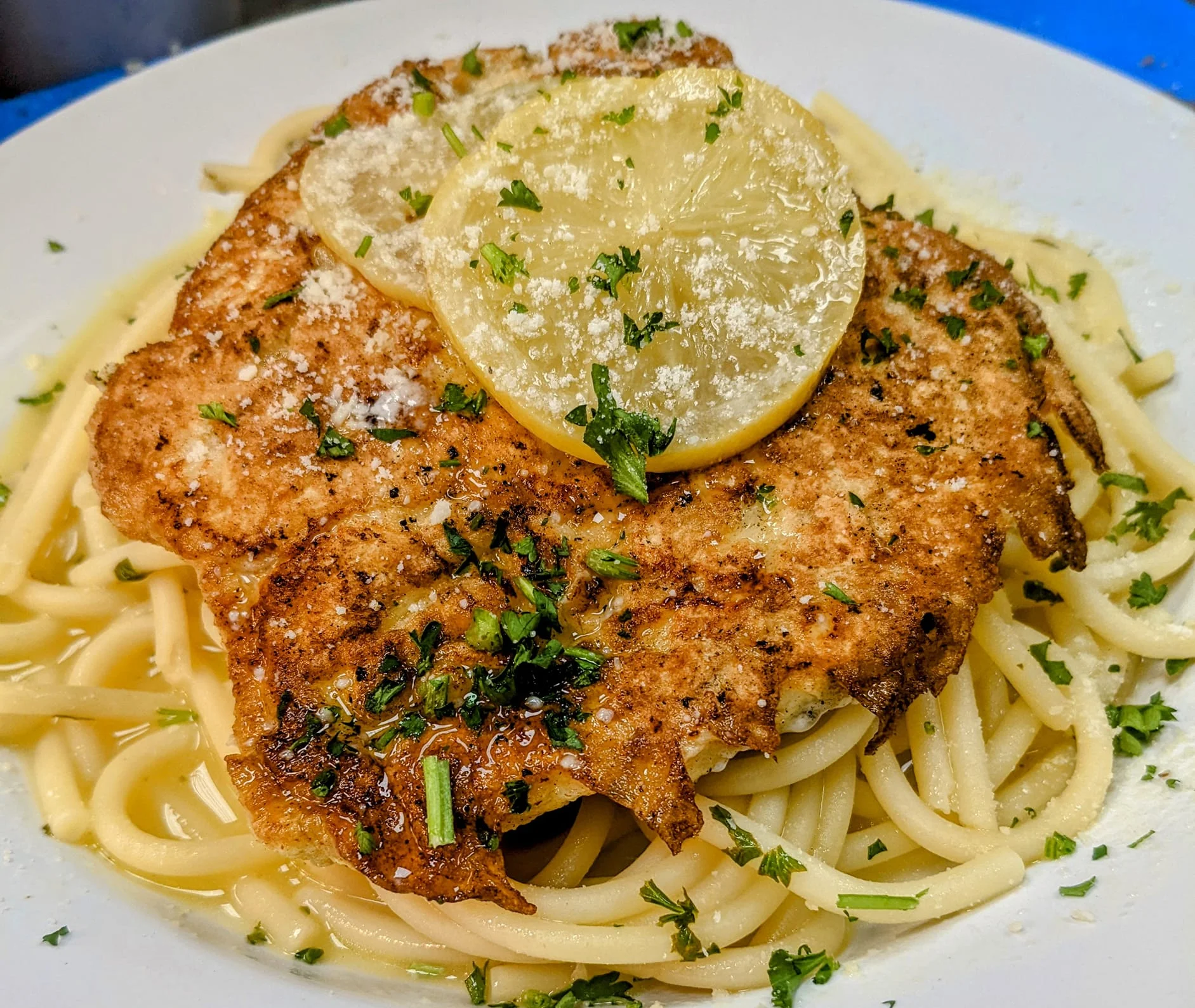 A plate of pasta entwined with shrimp, garnished with fresh herbs and lemon slices.