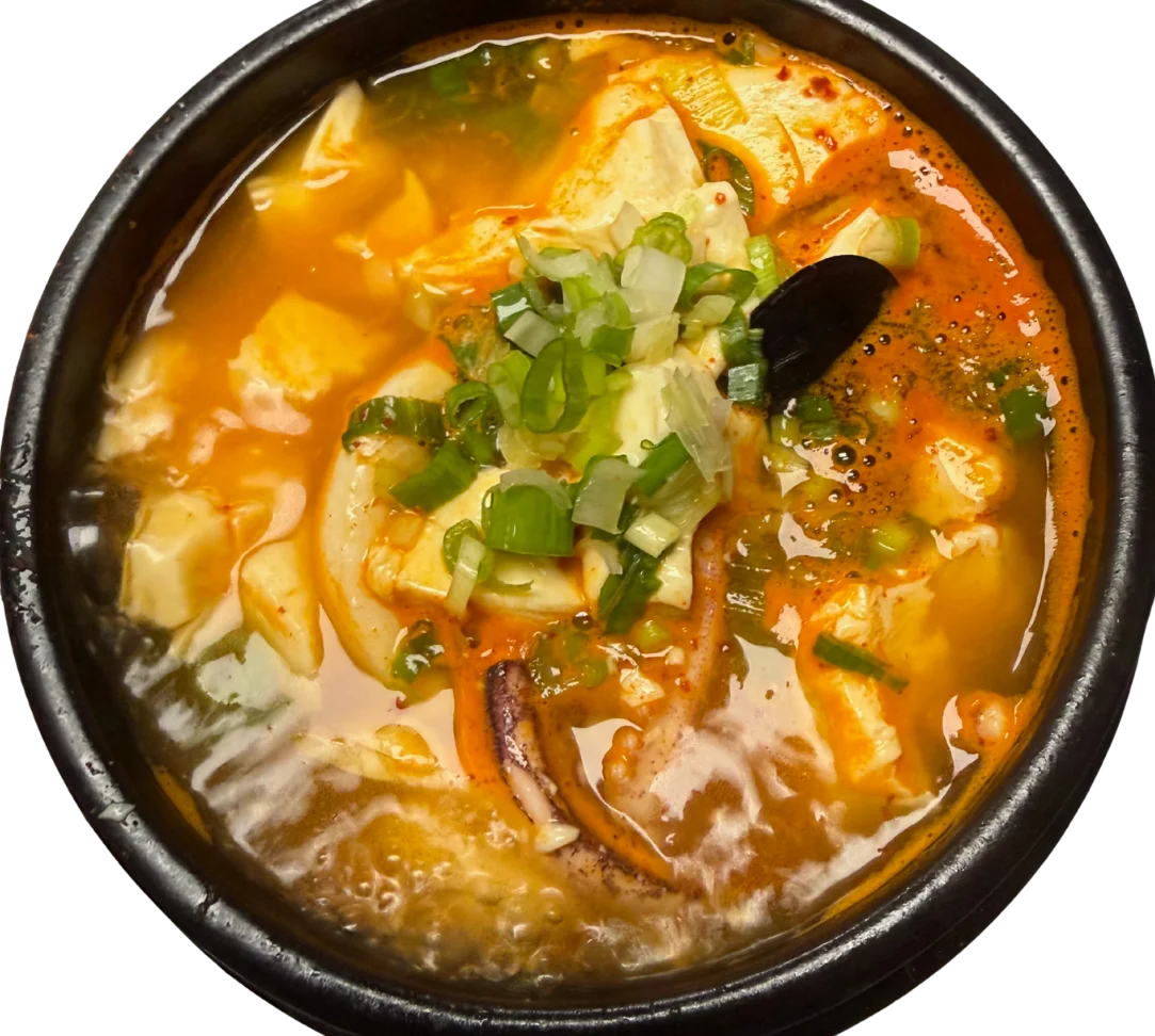 A steaming bowl of spicy soup with tofu, vegetables, and green onions.