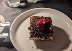 A slice of dessert featuring layers of chocolate cake with a berry on top, served on a white plate.