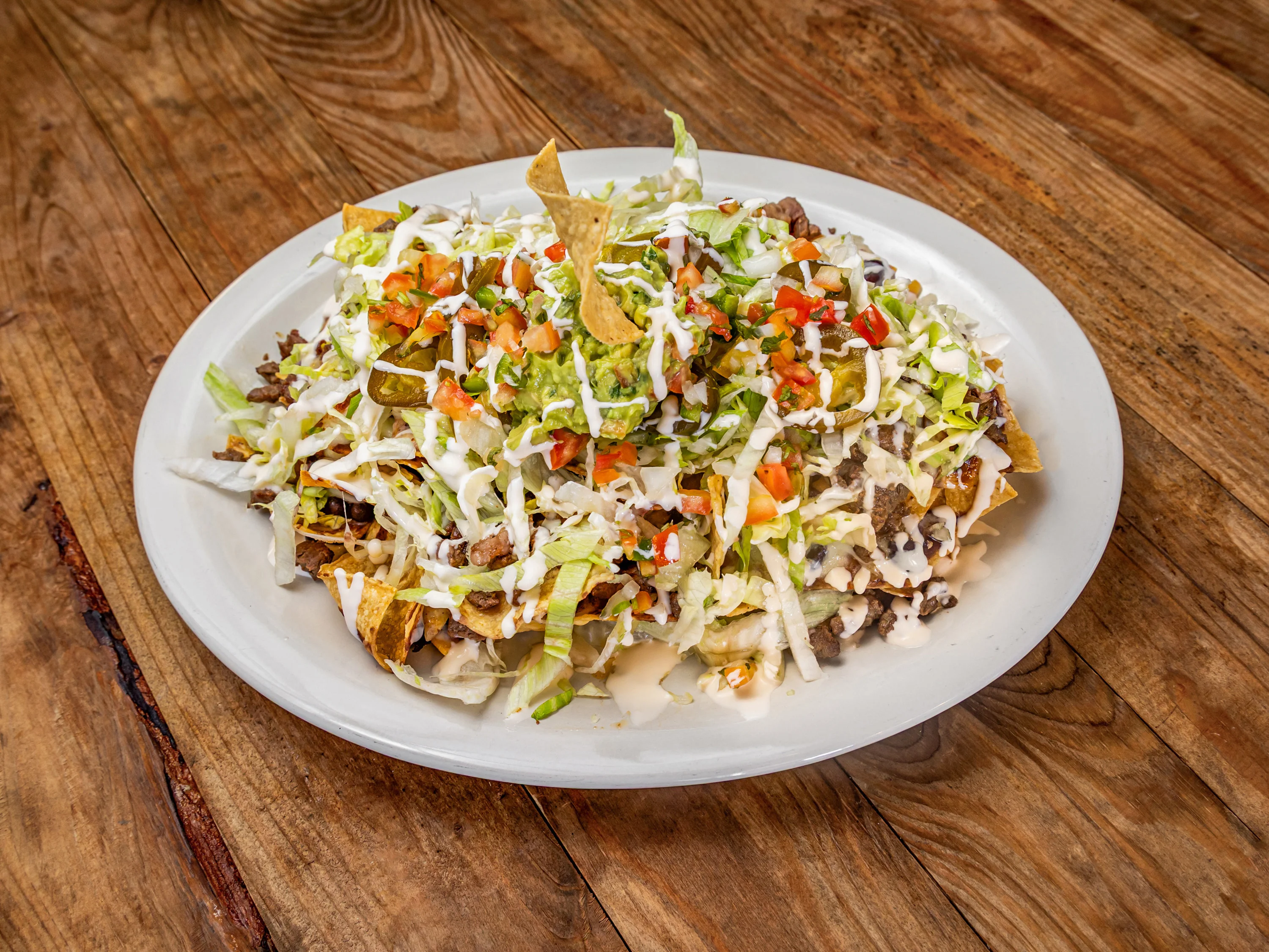 A plate of nachos topped with chopped lettuce, tomatoes, guacamole, and drizzled with sour cream over crispy tortilla chips.