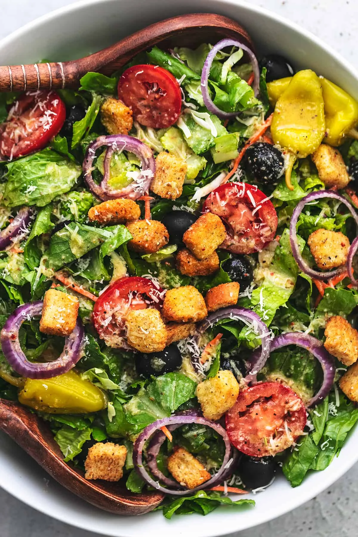A fresh salad featuring a variety of greens, cherry tomatoes, olives, red onion, and croutons, garnished with cheese.
