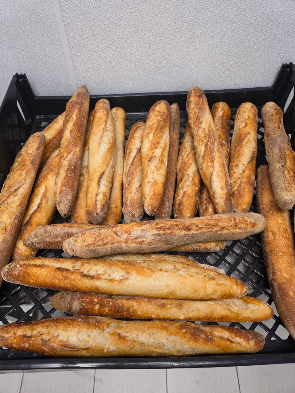 A collection of freshly baked baguettes arranged in a crate, showcasing their rustic texture and color.