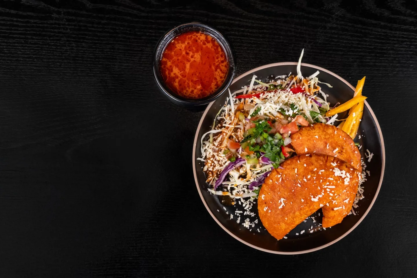 A colorful plate with crispy tacos, fresh salad, and a side of vibrant drink, showcasing a blend of flavors and textures.