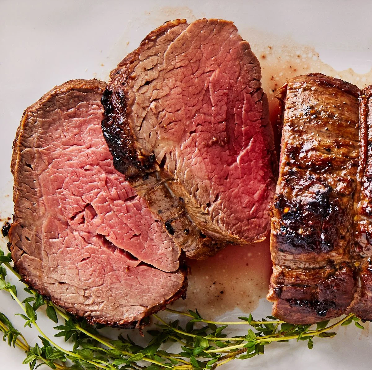 Sliced roast beef with herbs on a white plate.