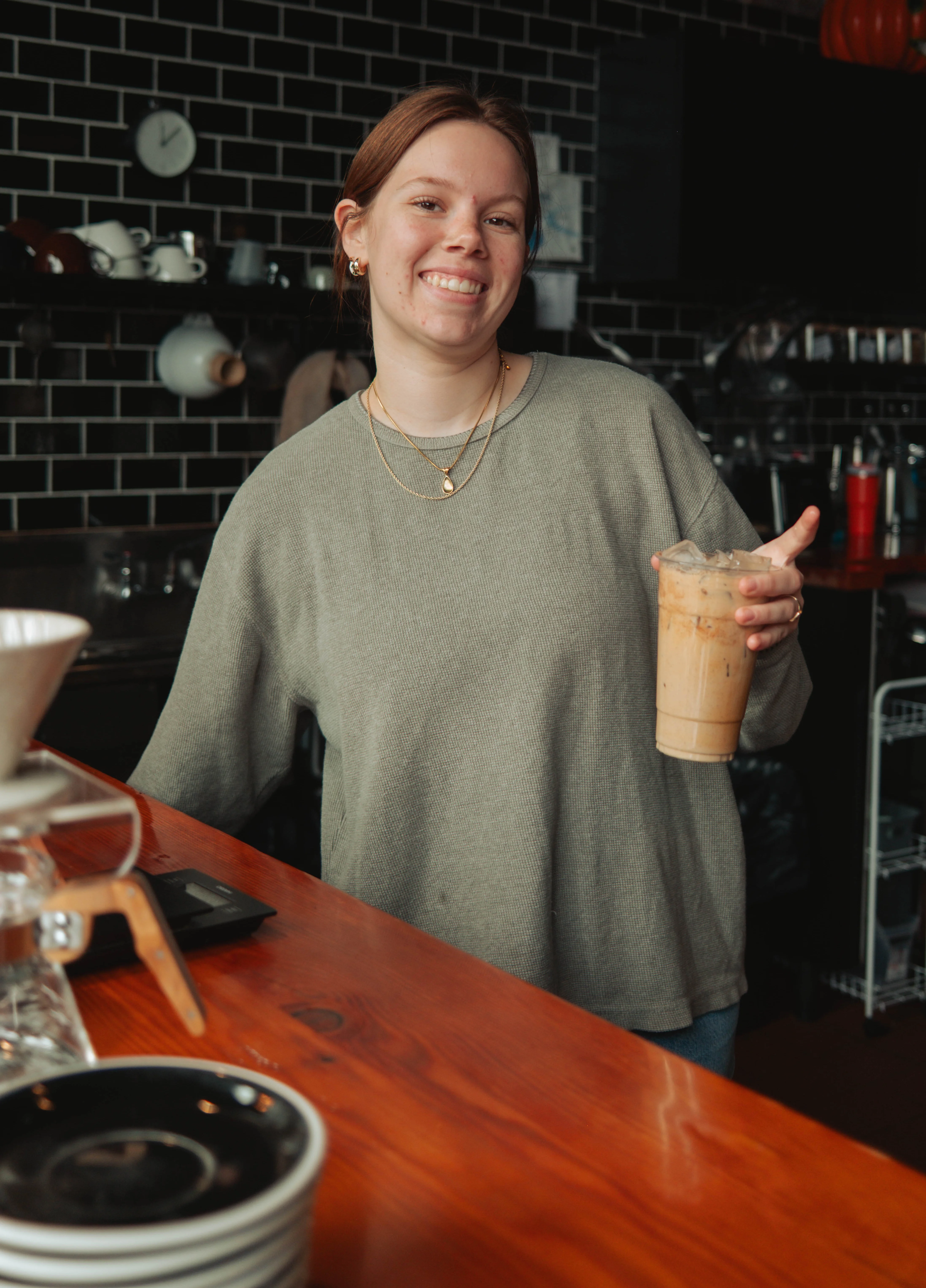 Barista smiling with iced coffee at a cozy café