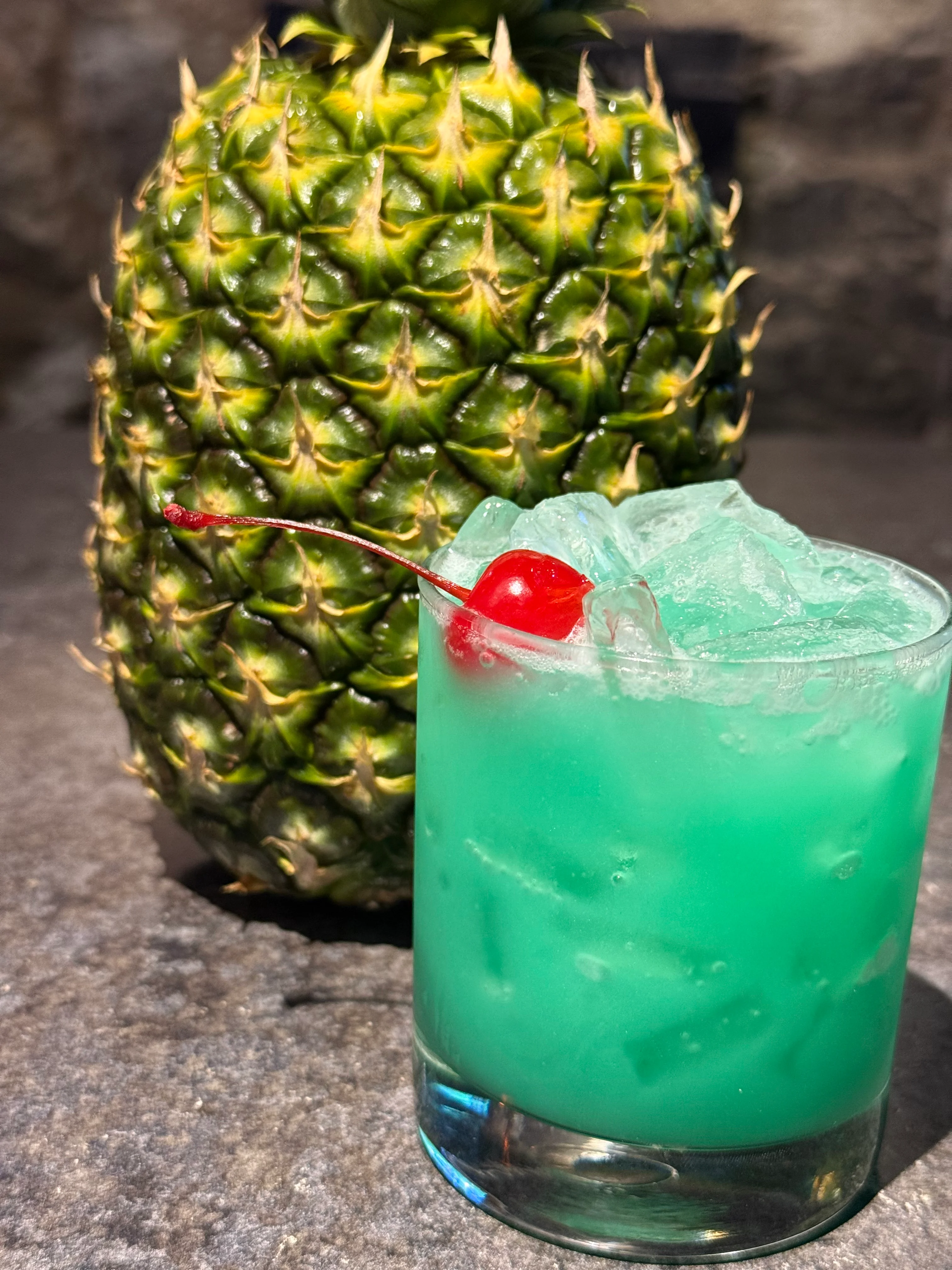 Tropical blue cocktail garnished with a cherry and fresh pineapple