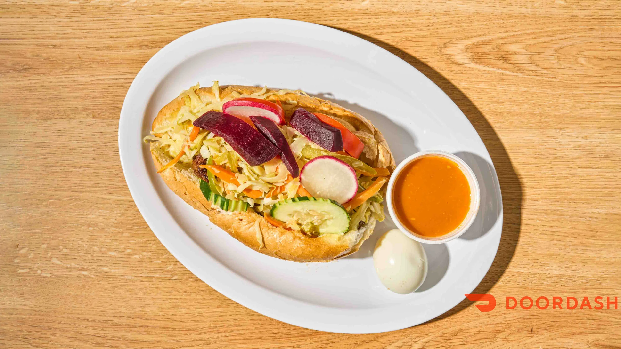 A sandwich with vegetables, sauce, and a boiled egg on a plate.