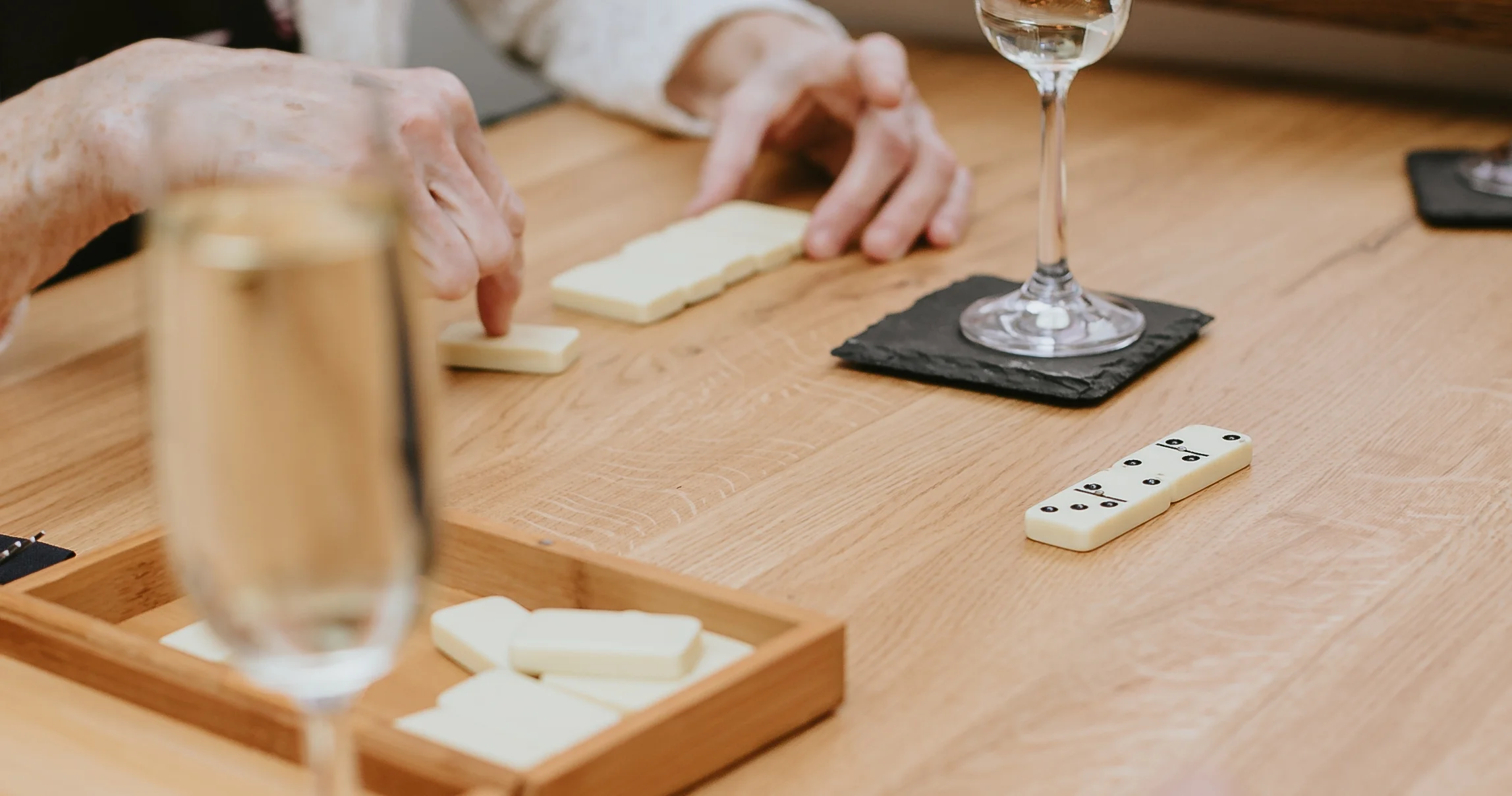 Group enjoying a game of dominoes with drinks on a wooden table