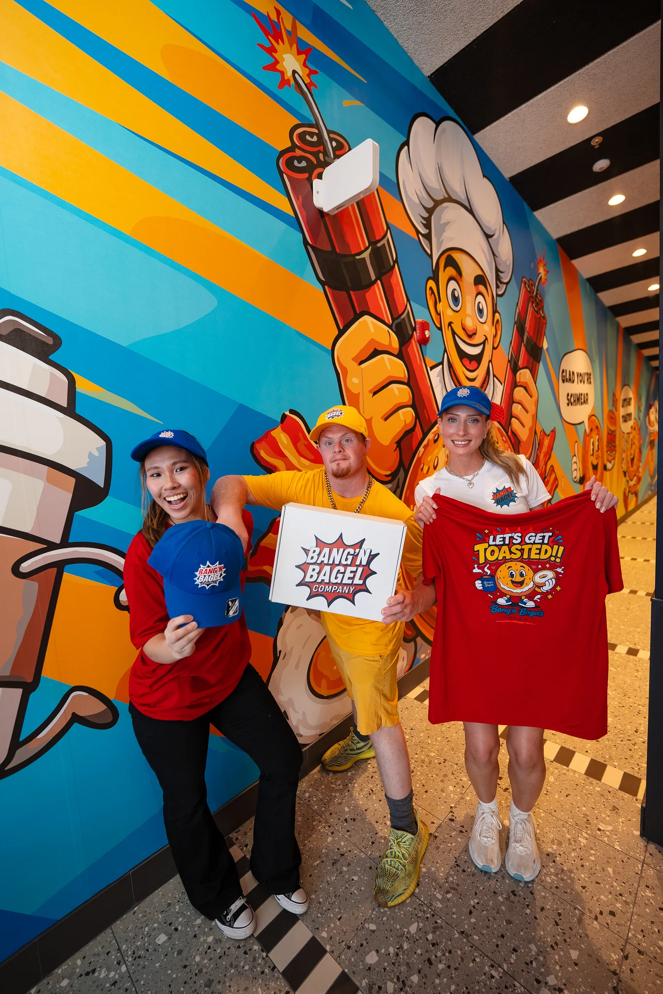 Staff showcasing Bang'n Bagel merchandise in a vibrant restaurant setting