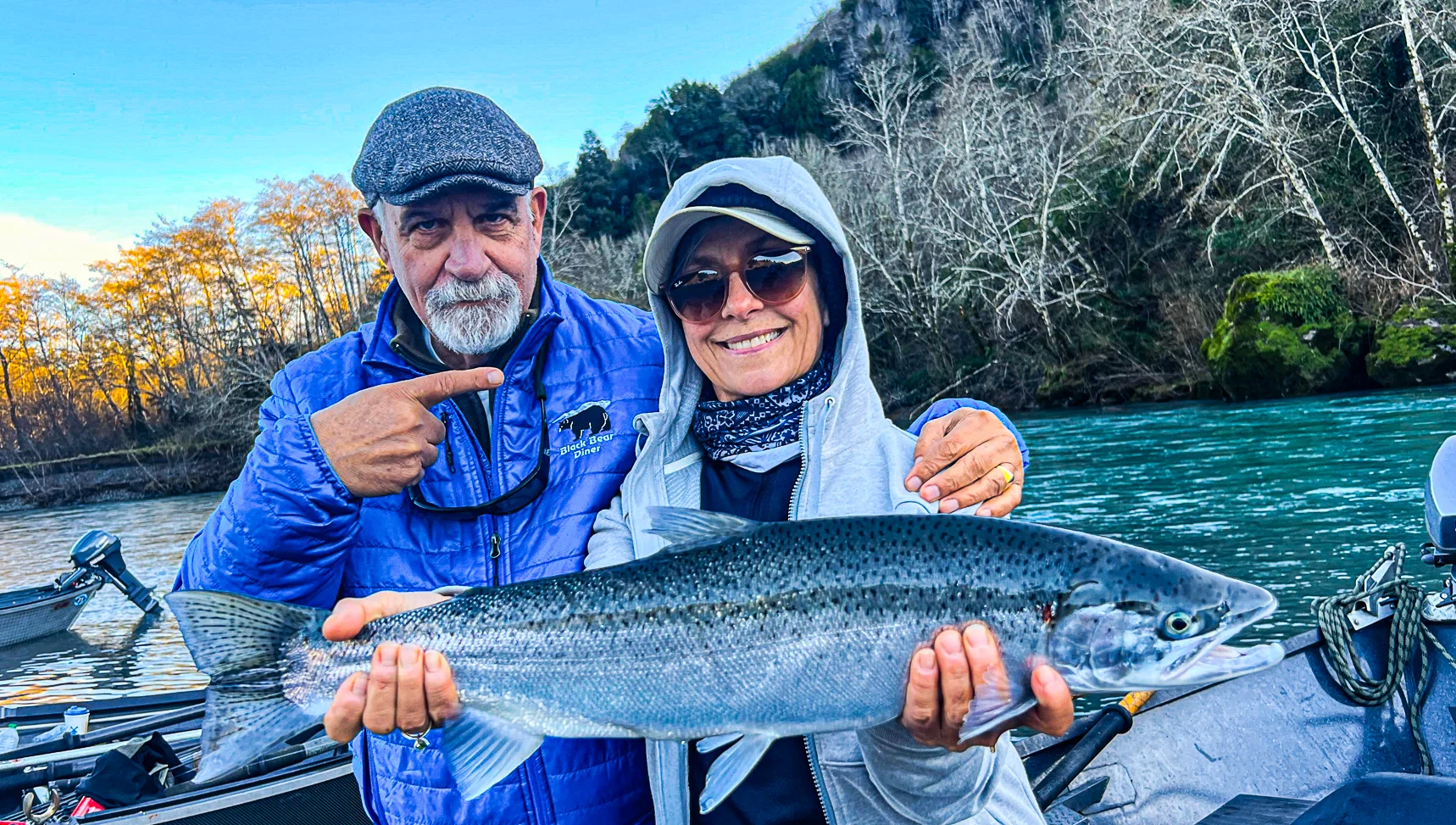 Anglers proudly holding a freshly caught salmon by the river