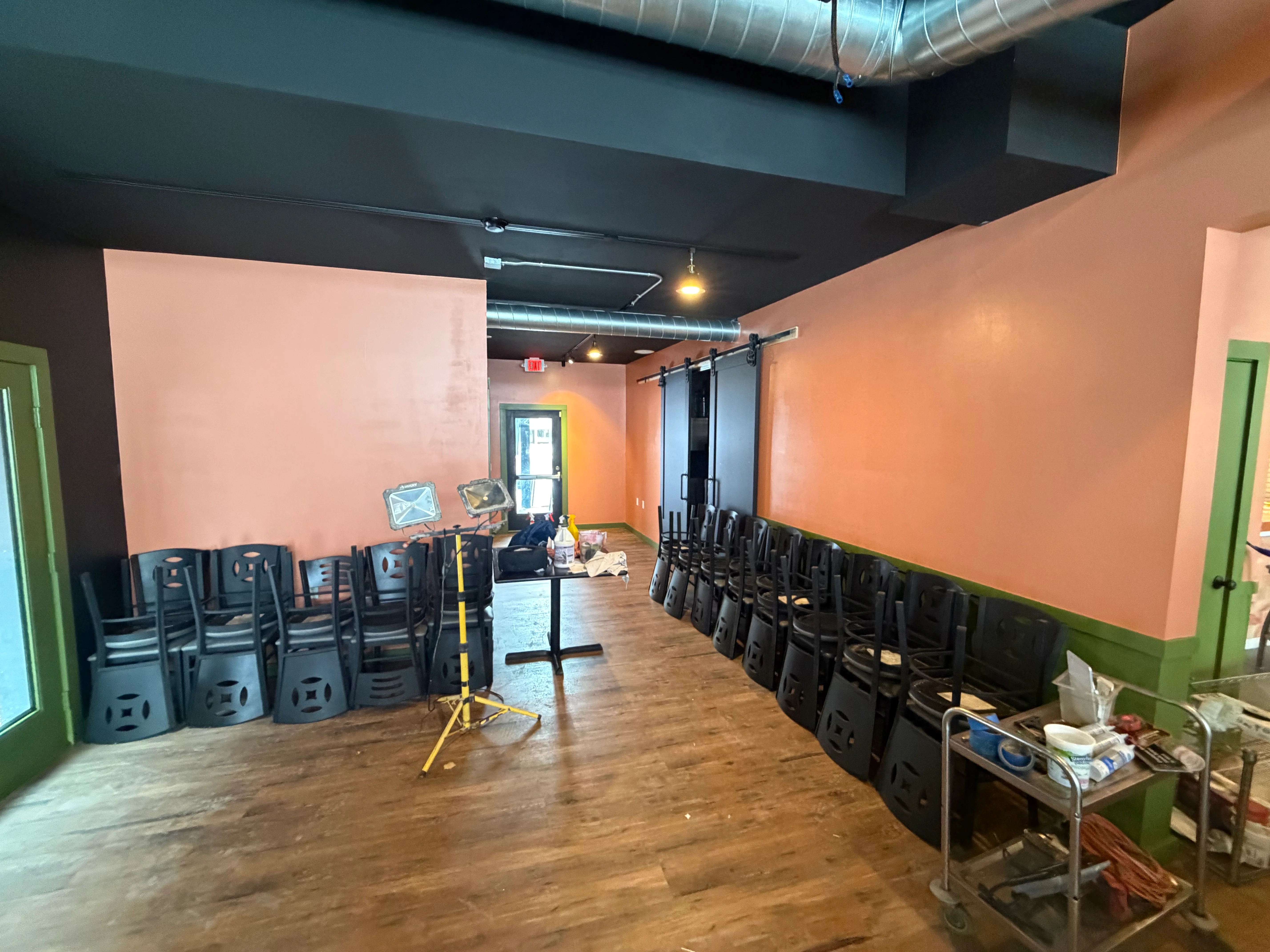 A cozy interior setup showcasing stacks of black chairs against orange walls, with a mix of furniture and tools placed around.