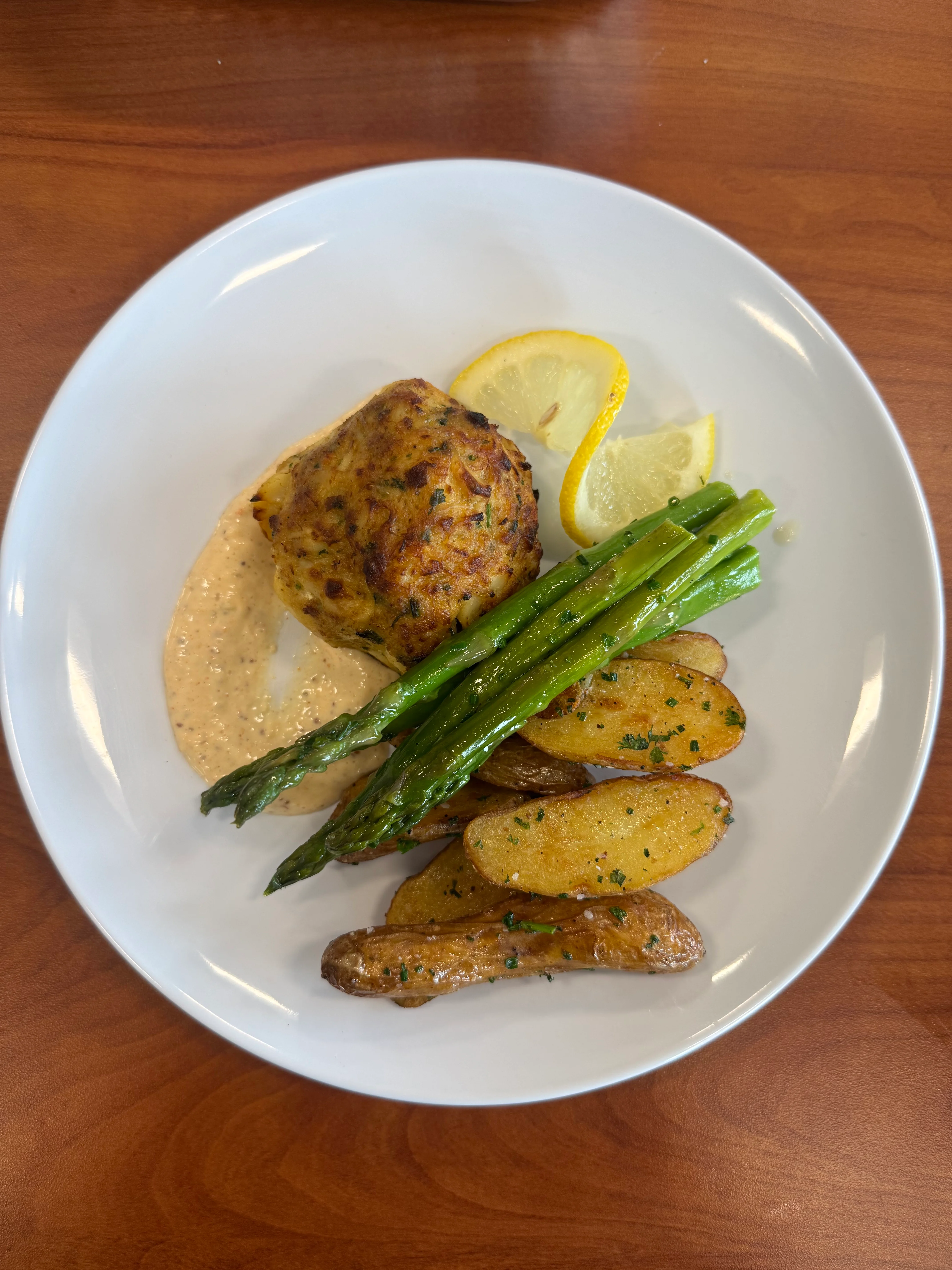 Plate of crab cake with asparagus, roasted potatoes, and lemon slices.