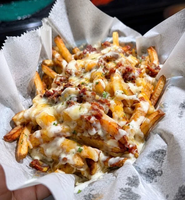 Loaded cheese fries topped with bacon bits and drizzled with sauce