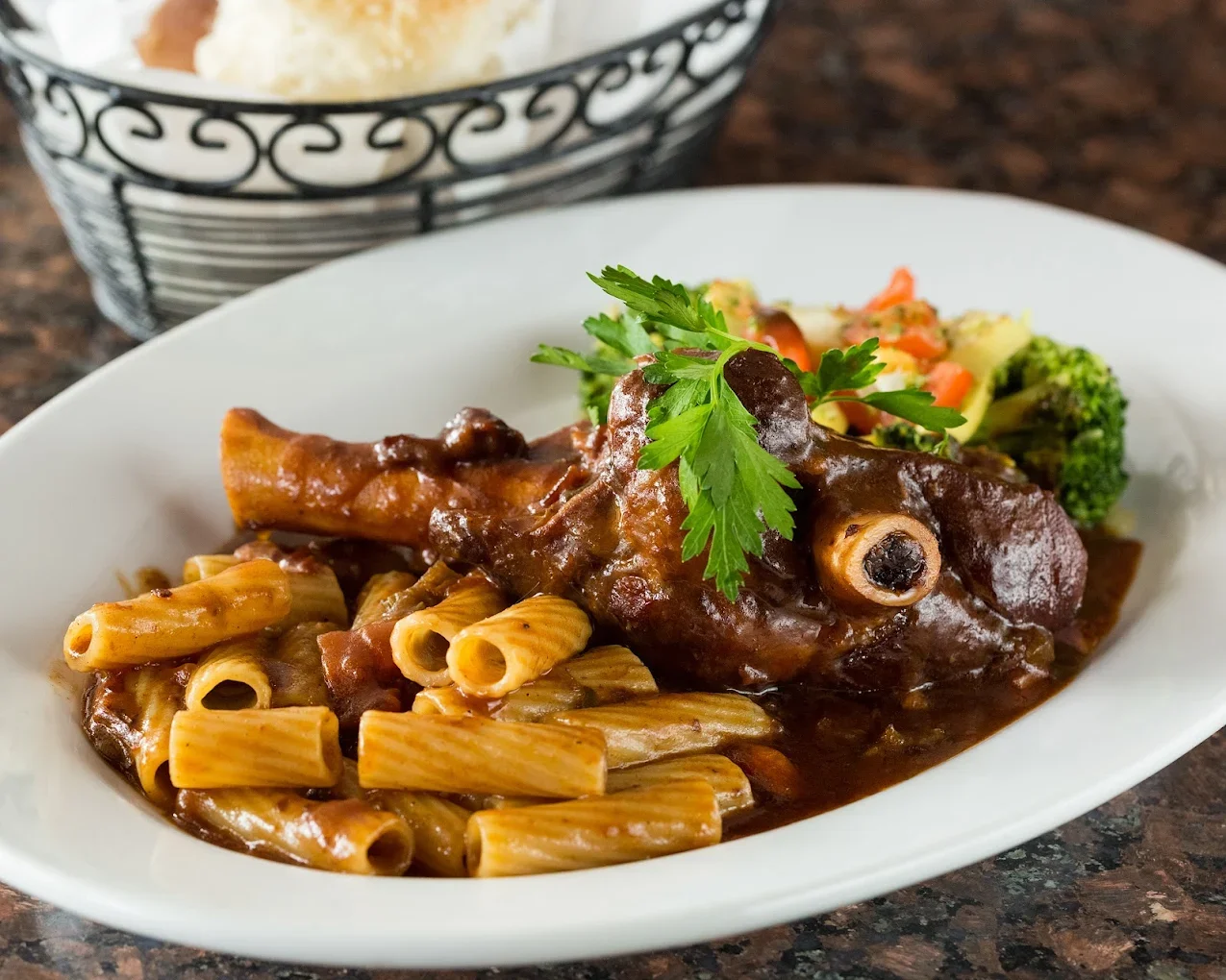 Braised beef shank served over rigatoni pasta with rich tomato sauce and fresh parsley garnish.