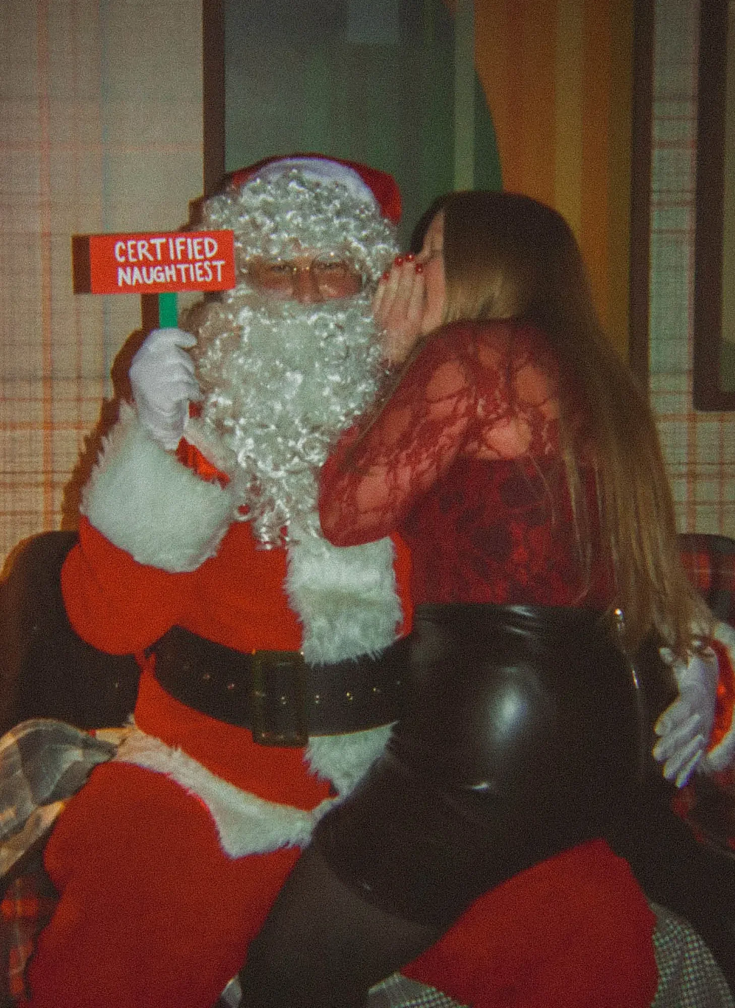 Person in Santa costume with a sign, posing with a woman in festive attire.