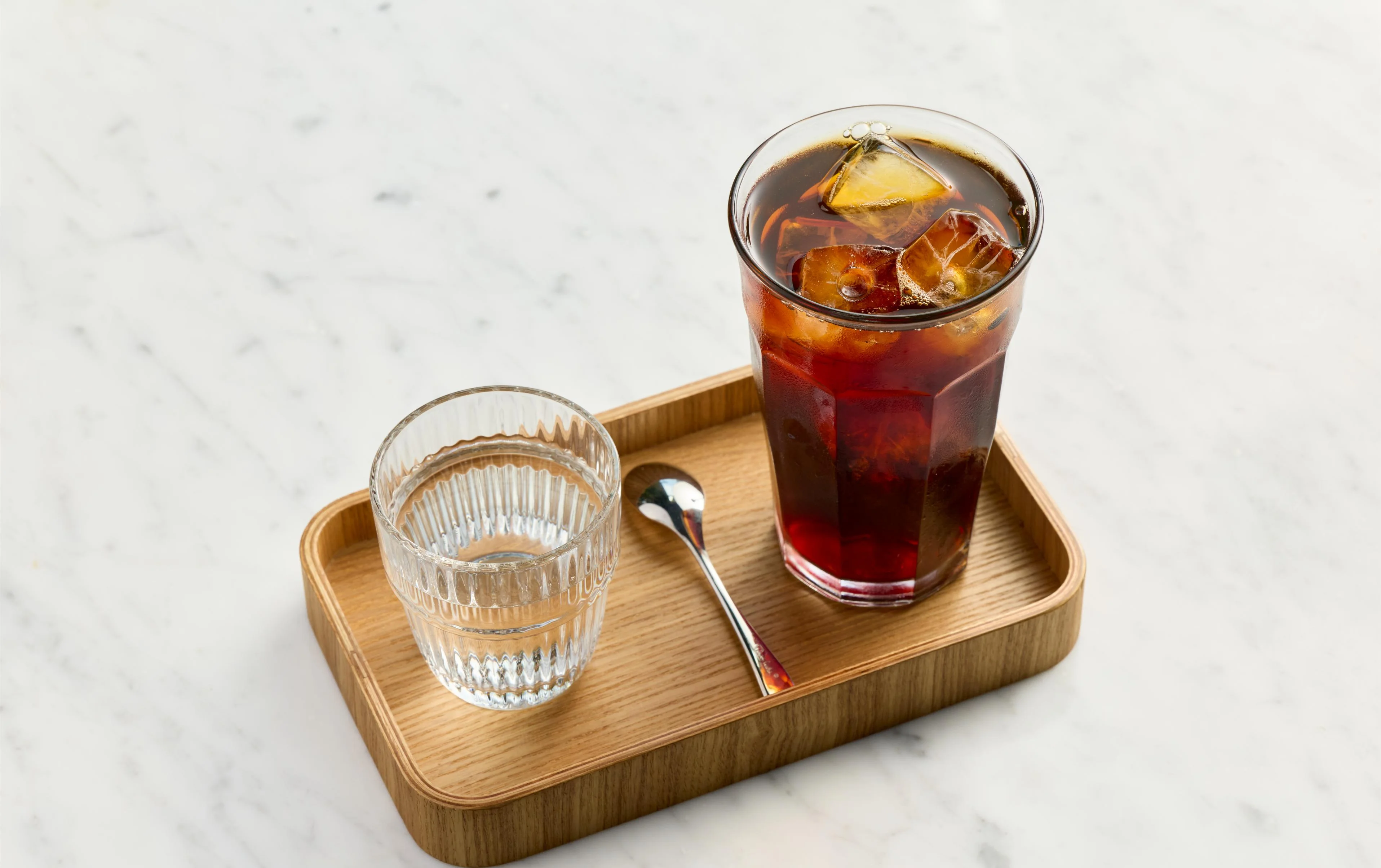 A glass of iced coffee with a side of water on a wooden tray.