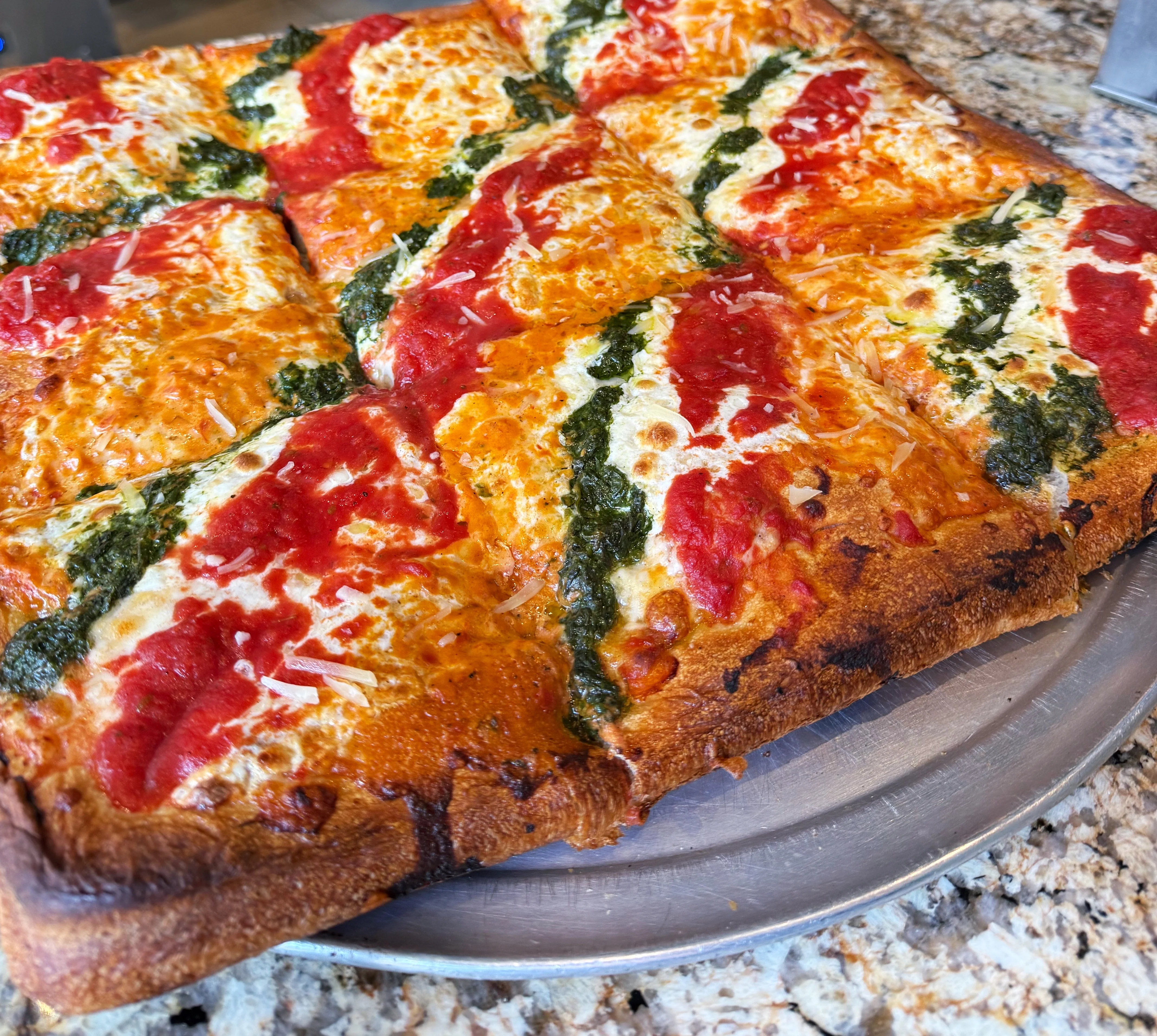 A square Sicilian MVP  pizza with a crispy crust, topped with marinara, vodka sauce, and pesto.