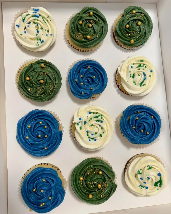 Another view of beautifully decorated cupcakes with swirl frosting in blue, green, and white, topped with colorful sprinkles, presented in a white box.