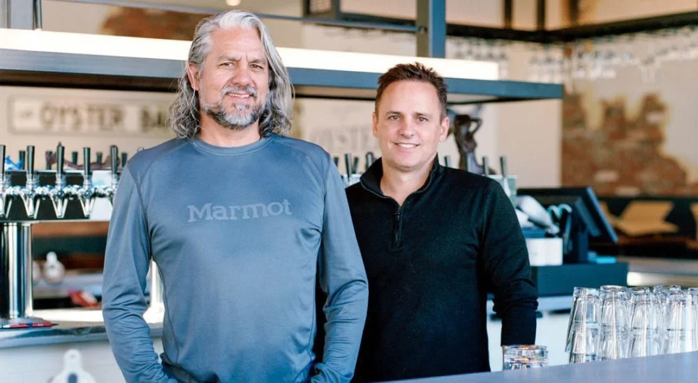 Two restaurateurs smiling behind a modern bar counter