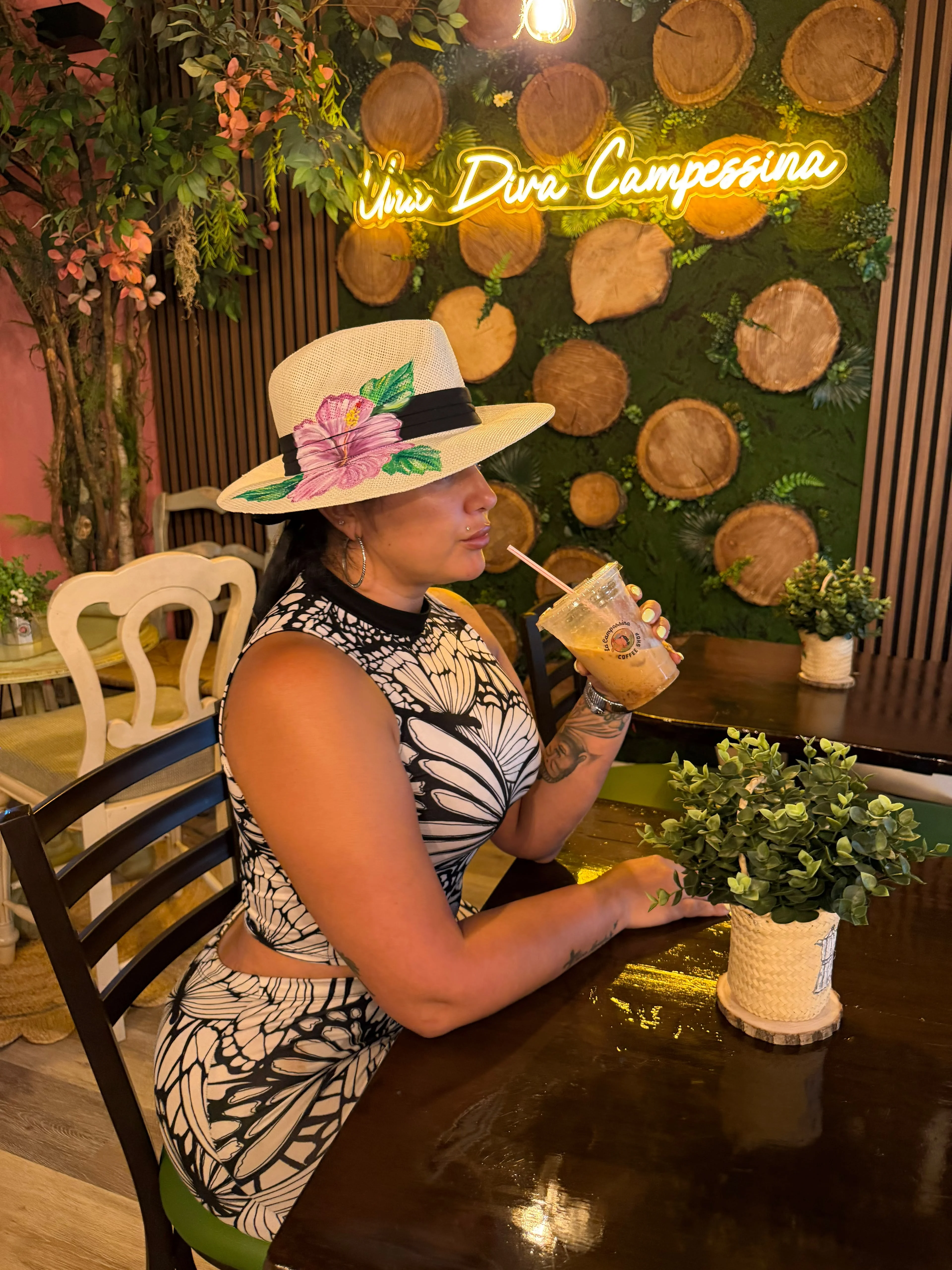 A woman in a stylish hat enjoys a drink in a cozy cafe setting with a green and wooden decor.