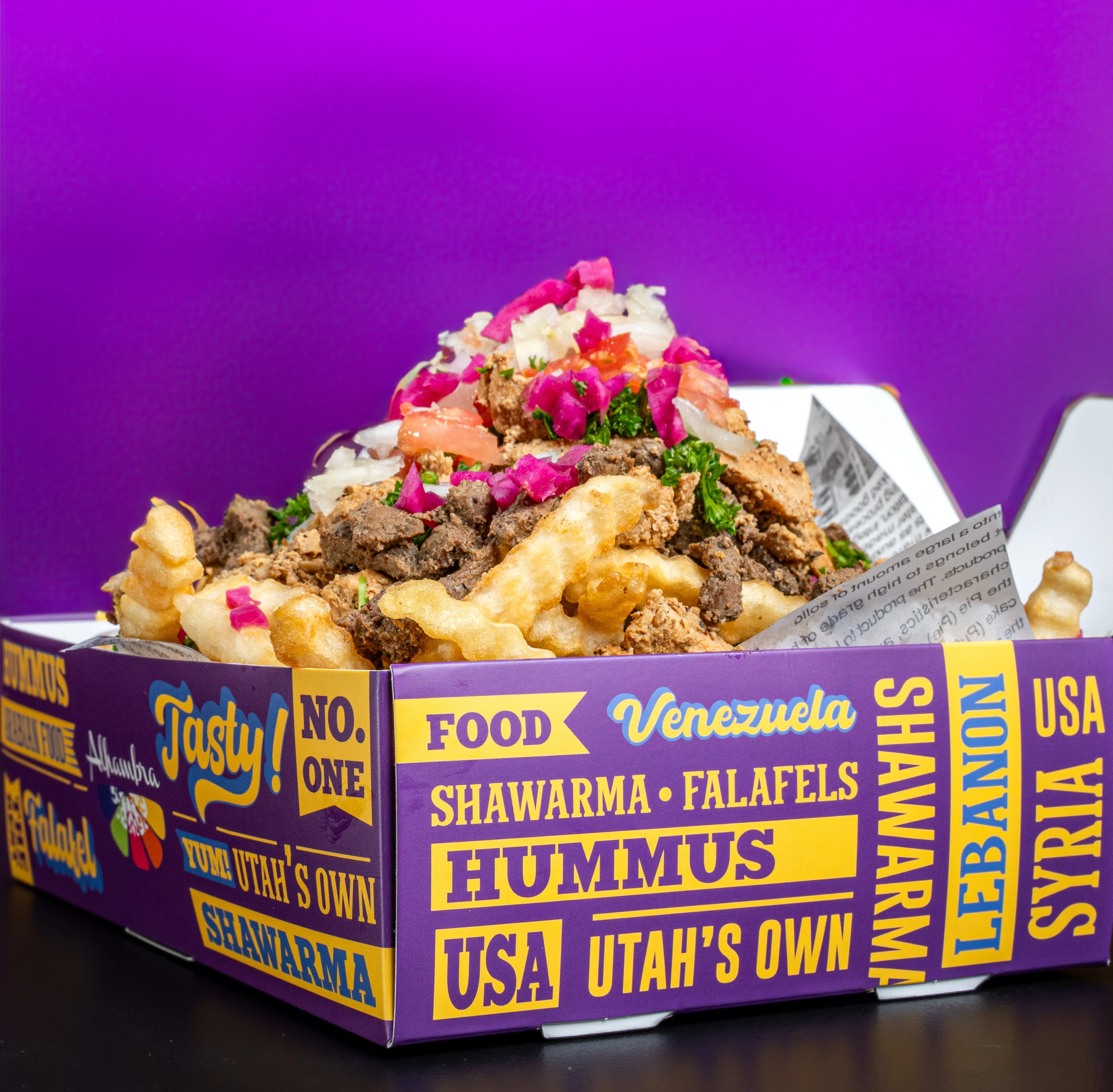 A colorful box filled with fries, shawarma, and fresh toppings.