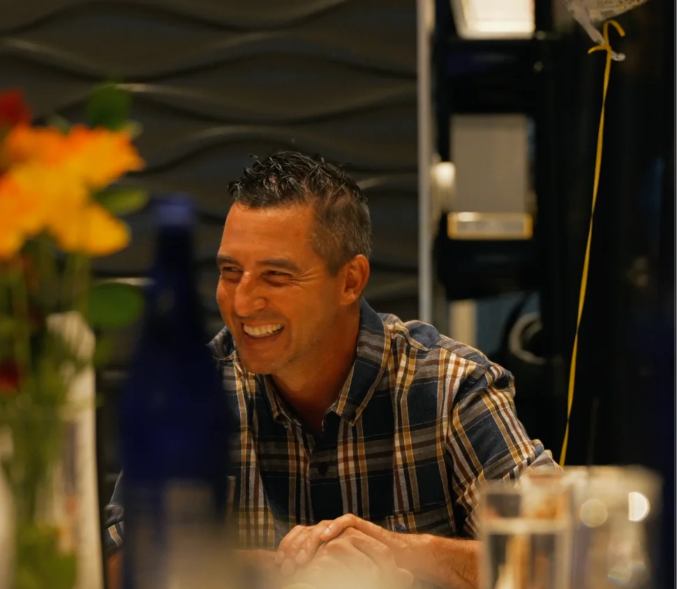 A smiling man at a restaurant table with flowers and a balloon.