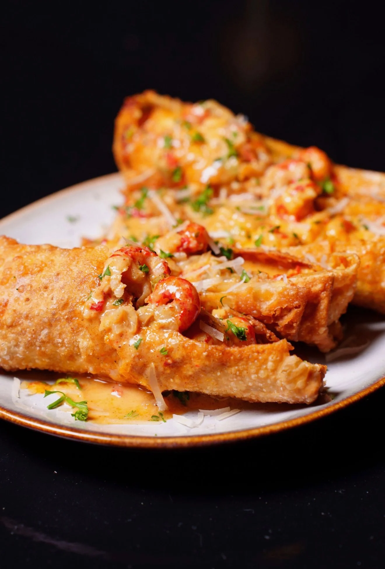 A close-up of golden, crispy shrimp-filled enchiladas topped with cheese and garnished with herbs on a plate.