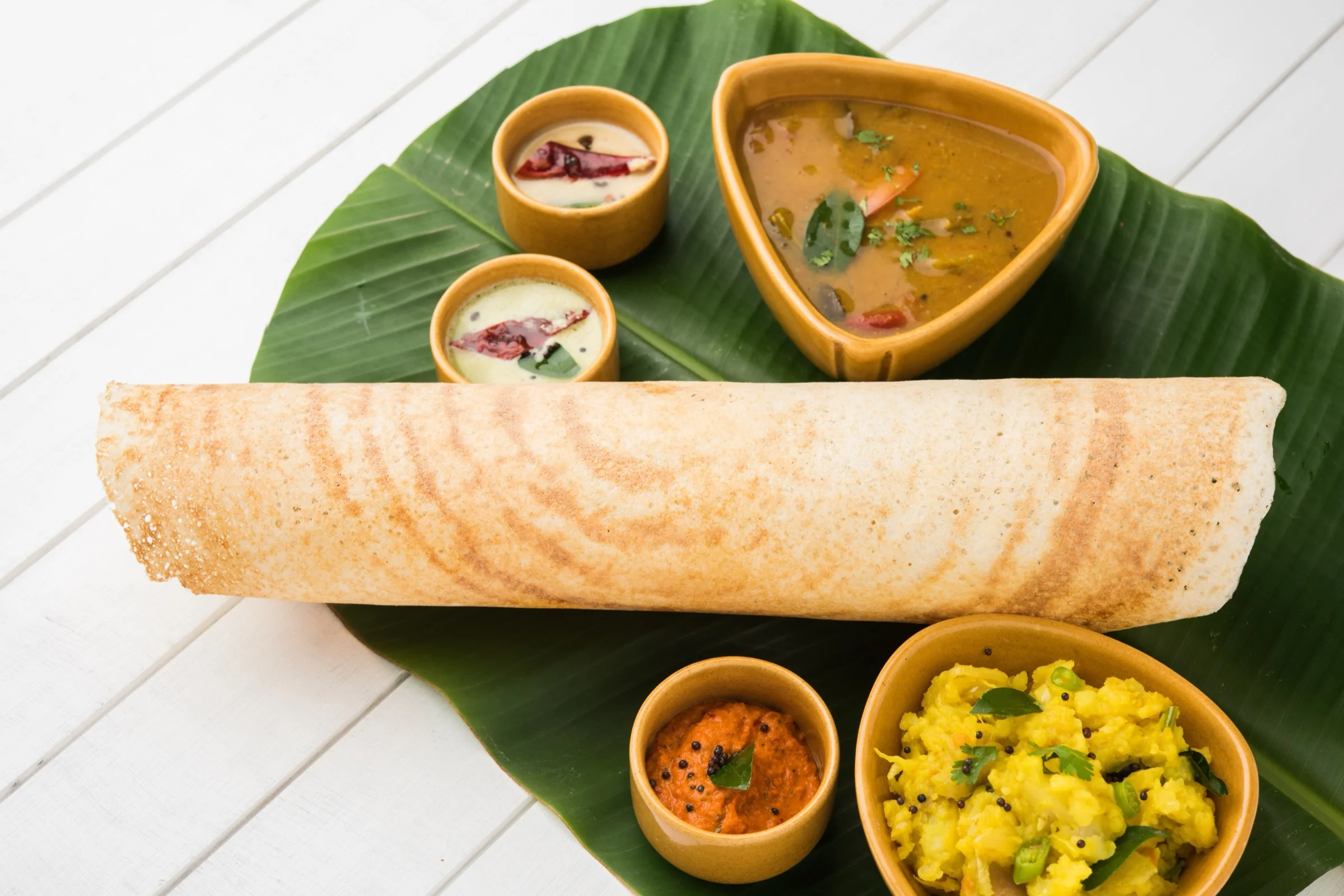 Masala dosa with sambar, chutneys and potato filling on a banana leaf