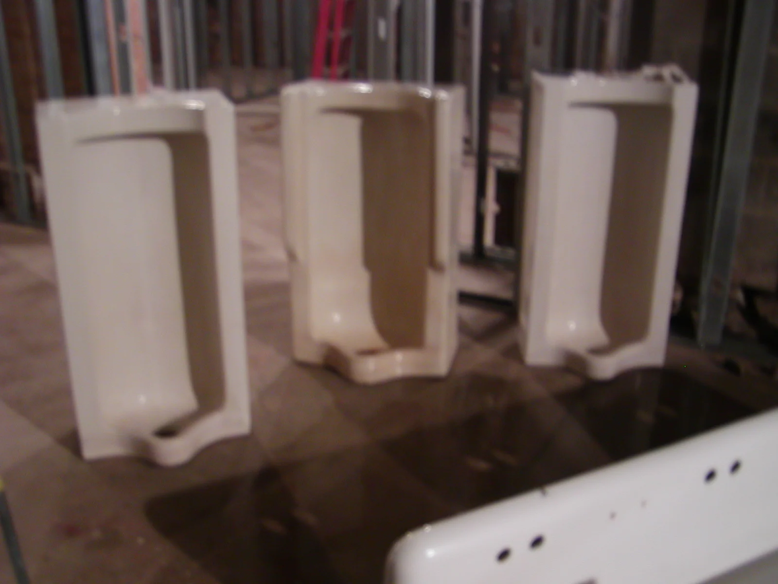 Three white urinals in a construction site setting