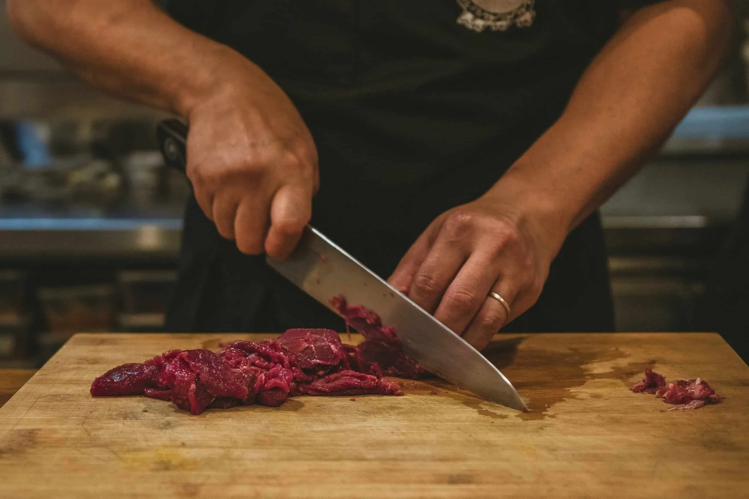 Chef slicing fresh beef on a wooden cutting board