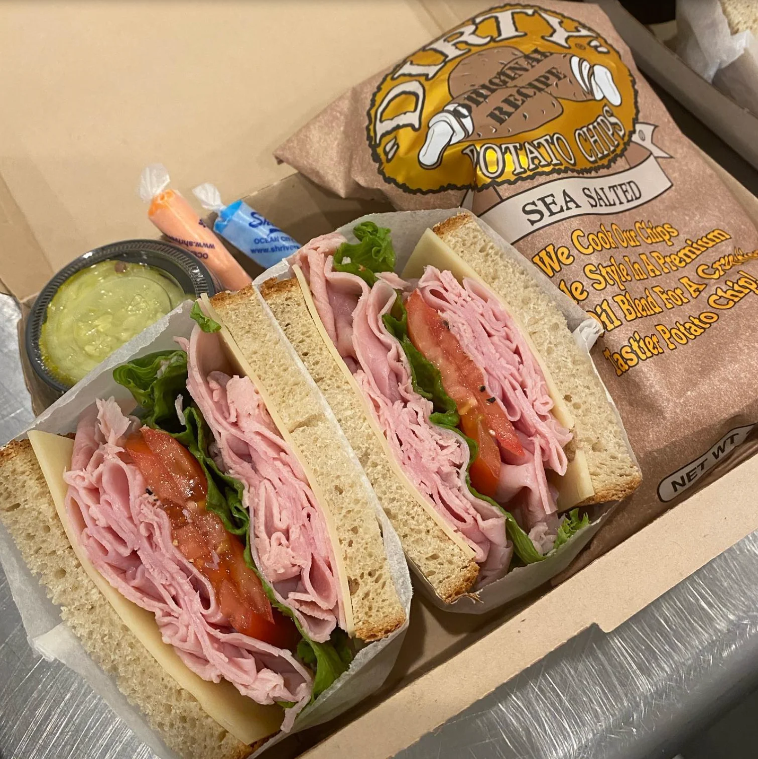 A sandwich with ham, lettuce, and tomato, served with potato chips and dip.