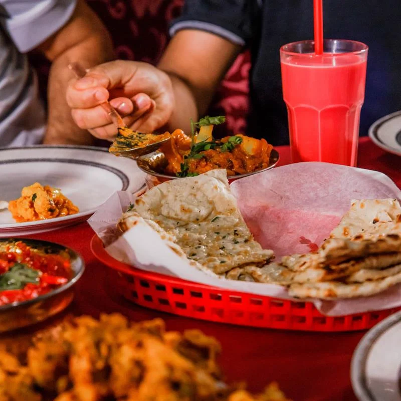 Guests enjoying a lively and exceptional dining experience at Mint Indian Restaurant, sharing a table filled with food and colorful cocktails.