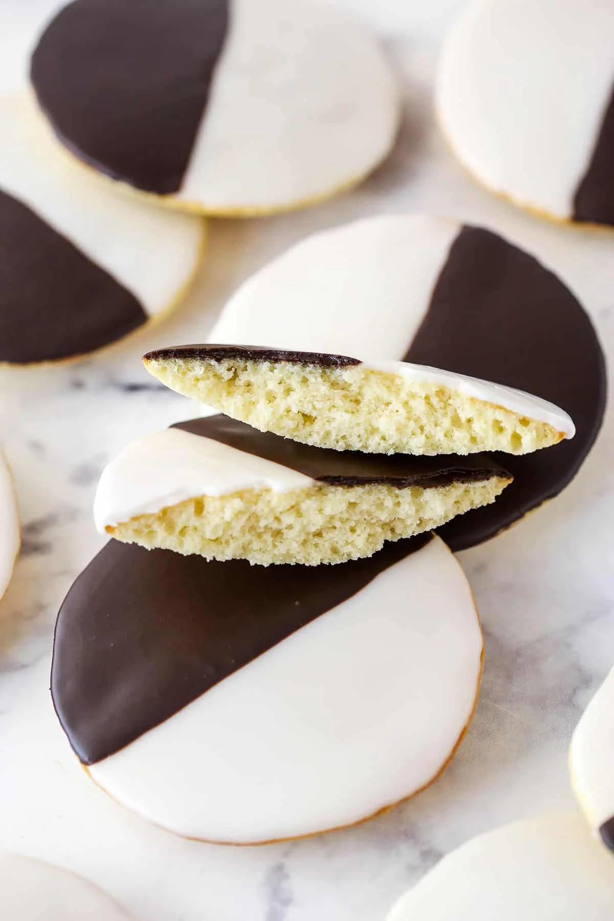Black and white iced cookies stacked on a marble surface.