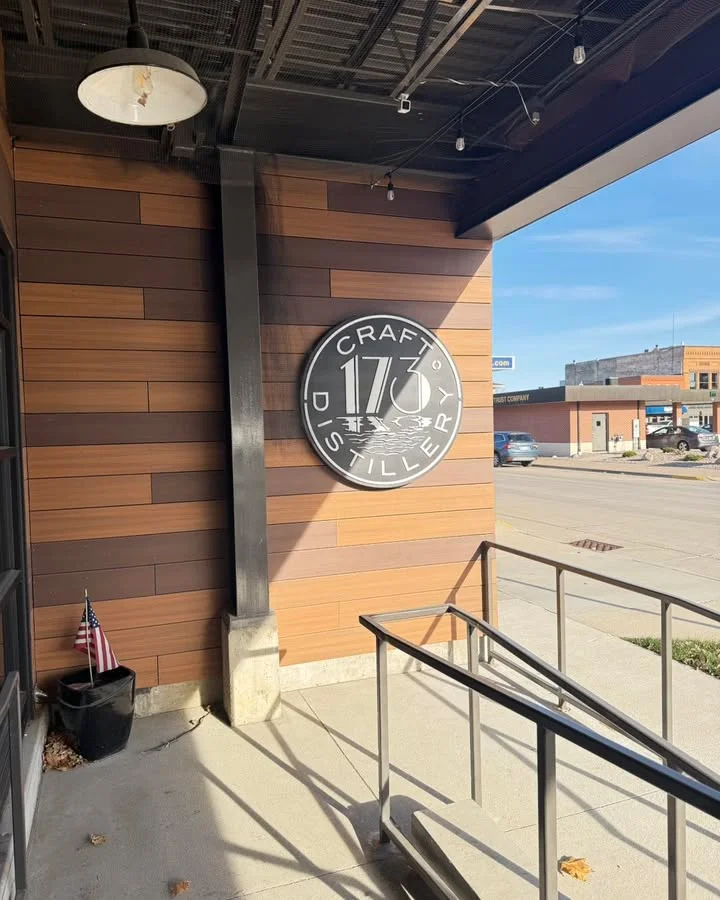 The exterior of a craft distillery with a modern wooden facade and a prominent logo sign.