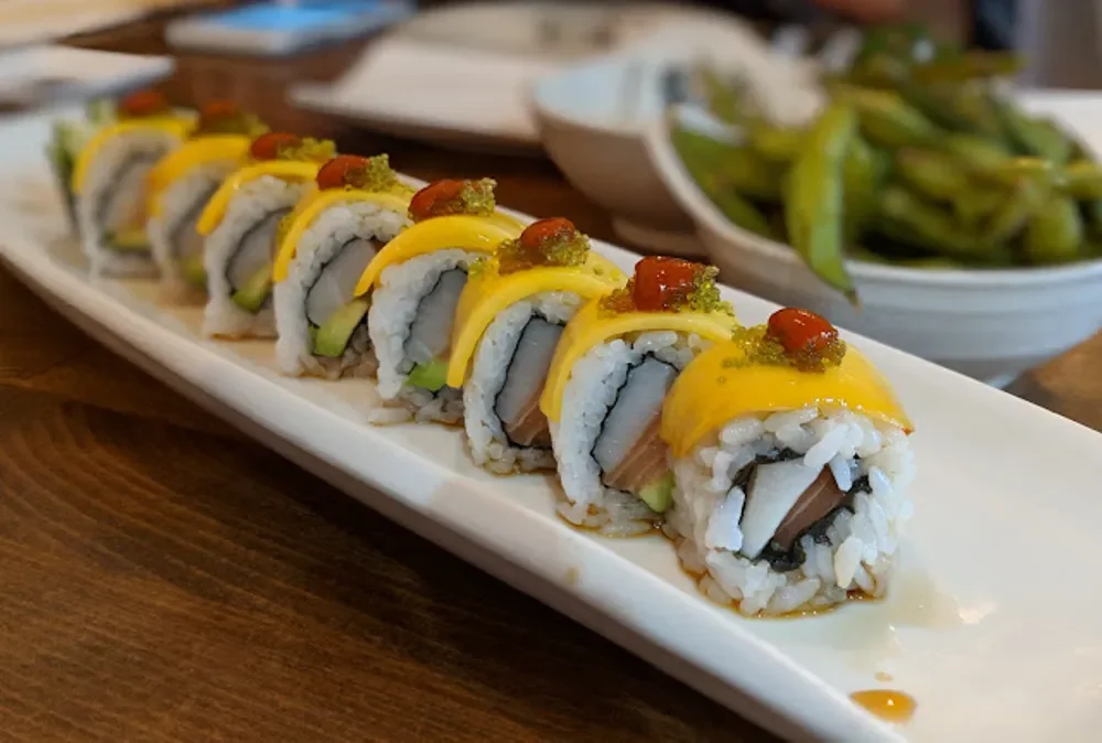 Colorful sushi rolls with mango and spicy sauce on a white plate