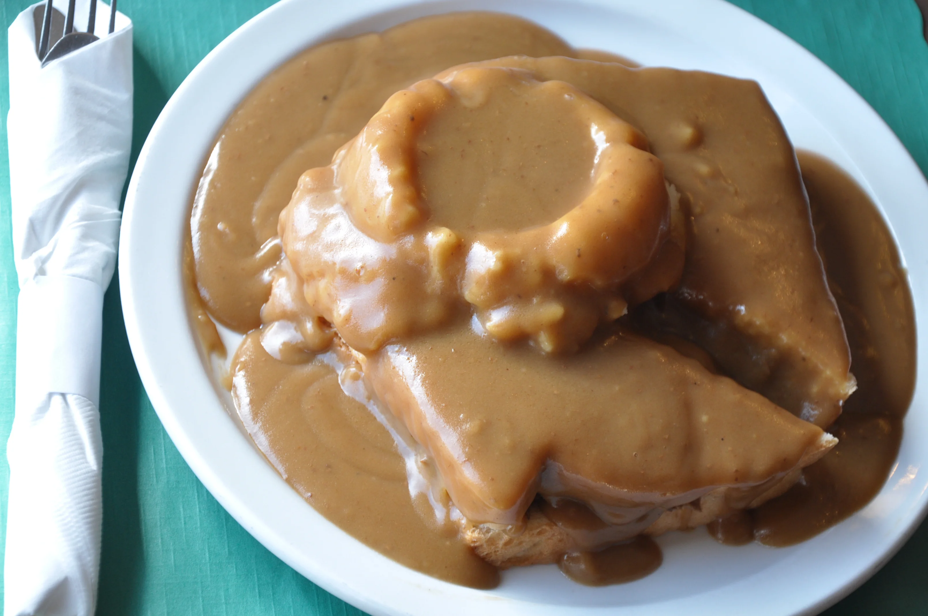A plate of bread covered in a thick, savory gravy, served with a round piece of bread stacked on top.
